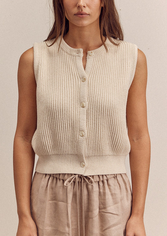A woman wearing a sleeveless cream colored sweater vest with button front.