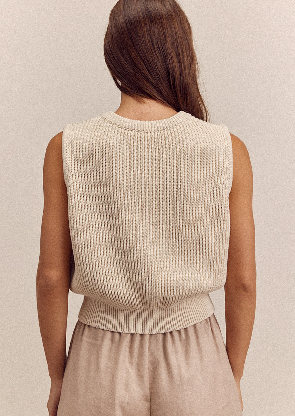 A woman wearing a sleeveless cream colored sweater vest with button front.