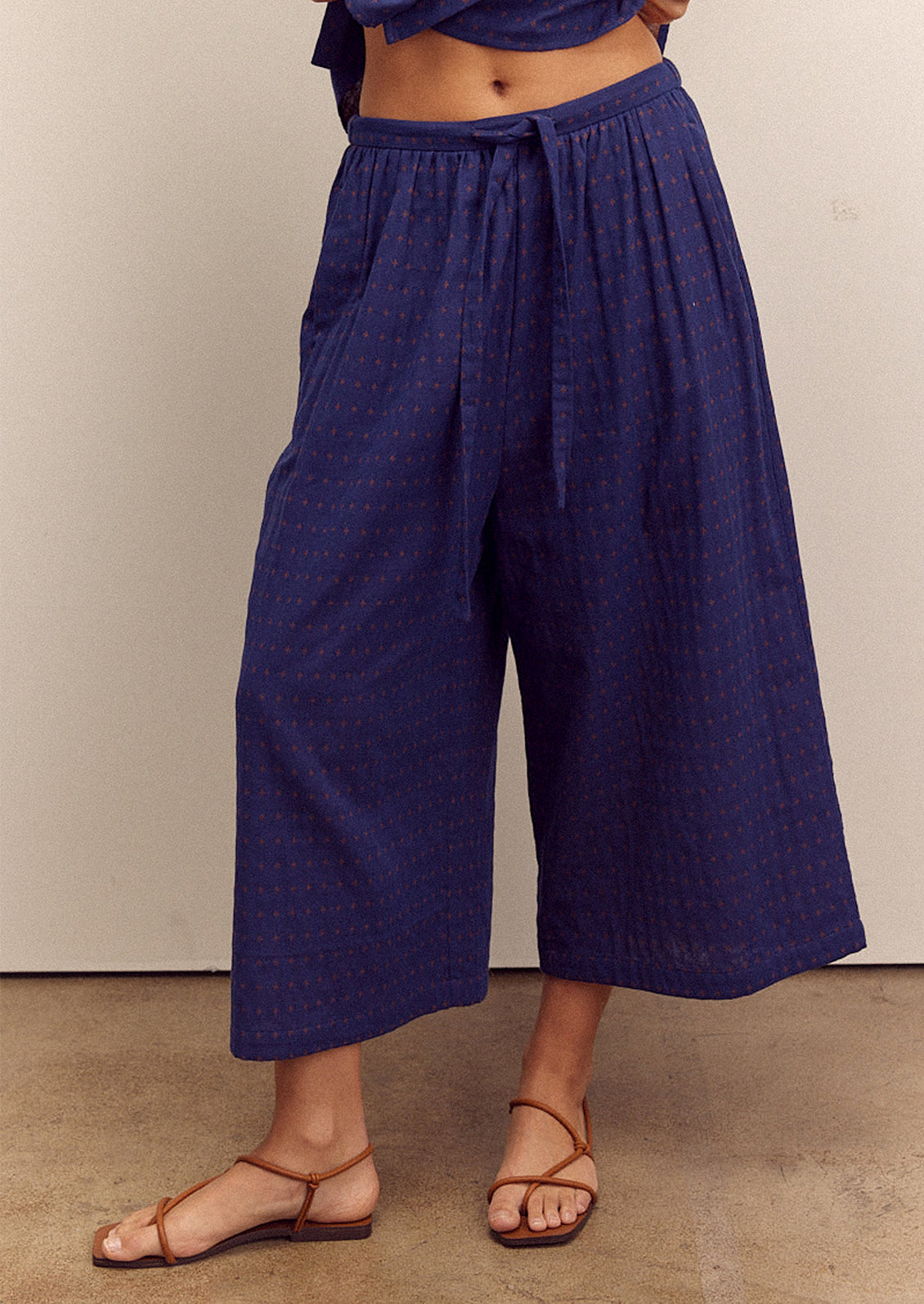 A person wearing a pair of cropped, wide leg pants in navy blue with tiny orange cross pattern.