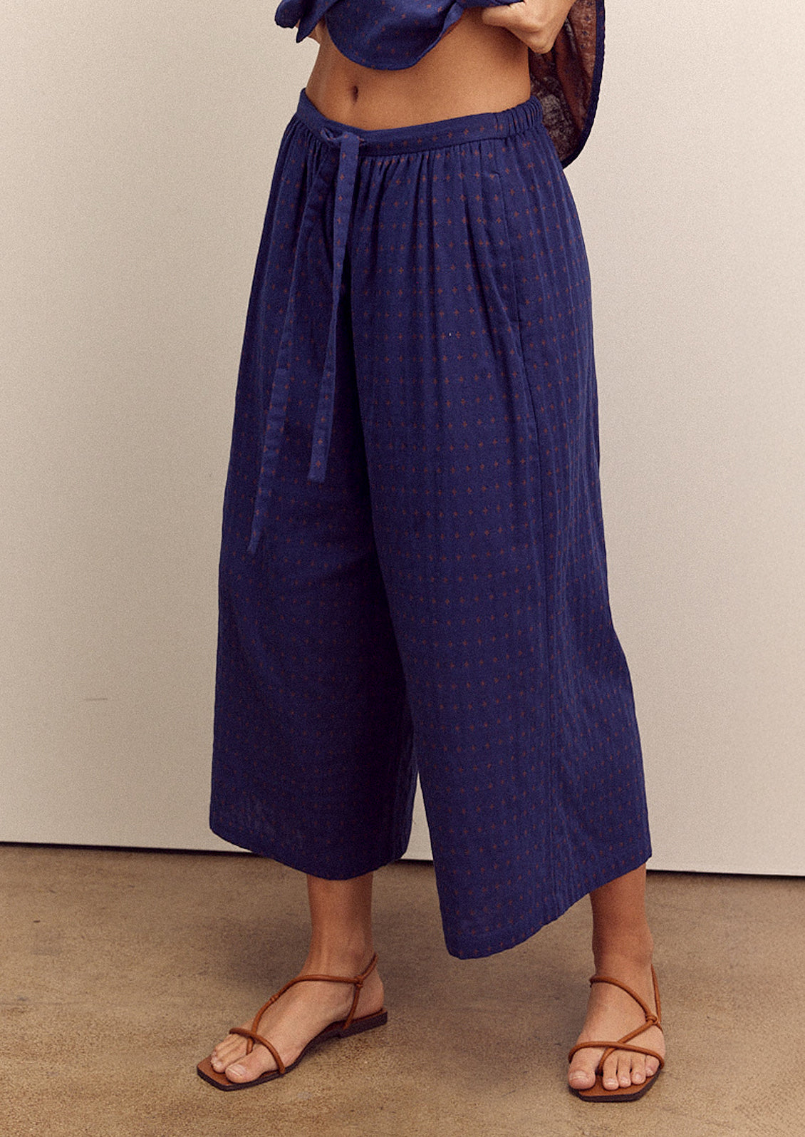 A person wearing a pair of cropped, wide leg pants in navy blue with tiny orange cross pattern.