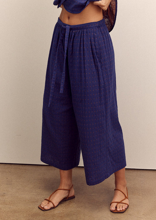 A person wearing a pair of cropped, wide leg pants in navy blue with tiny orange cross pattern.