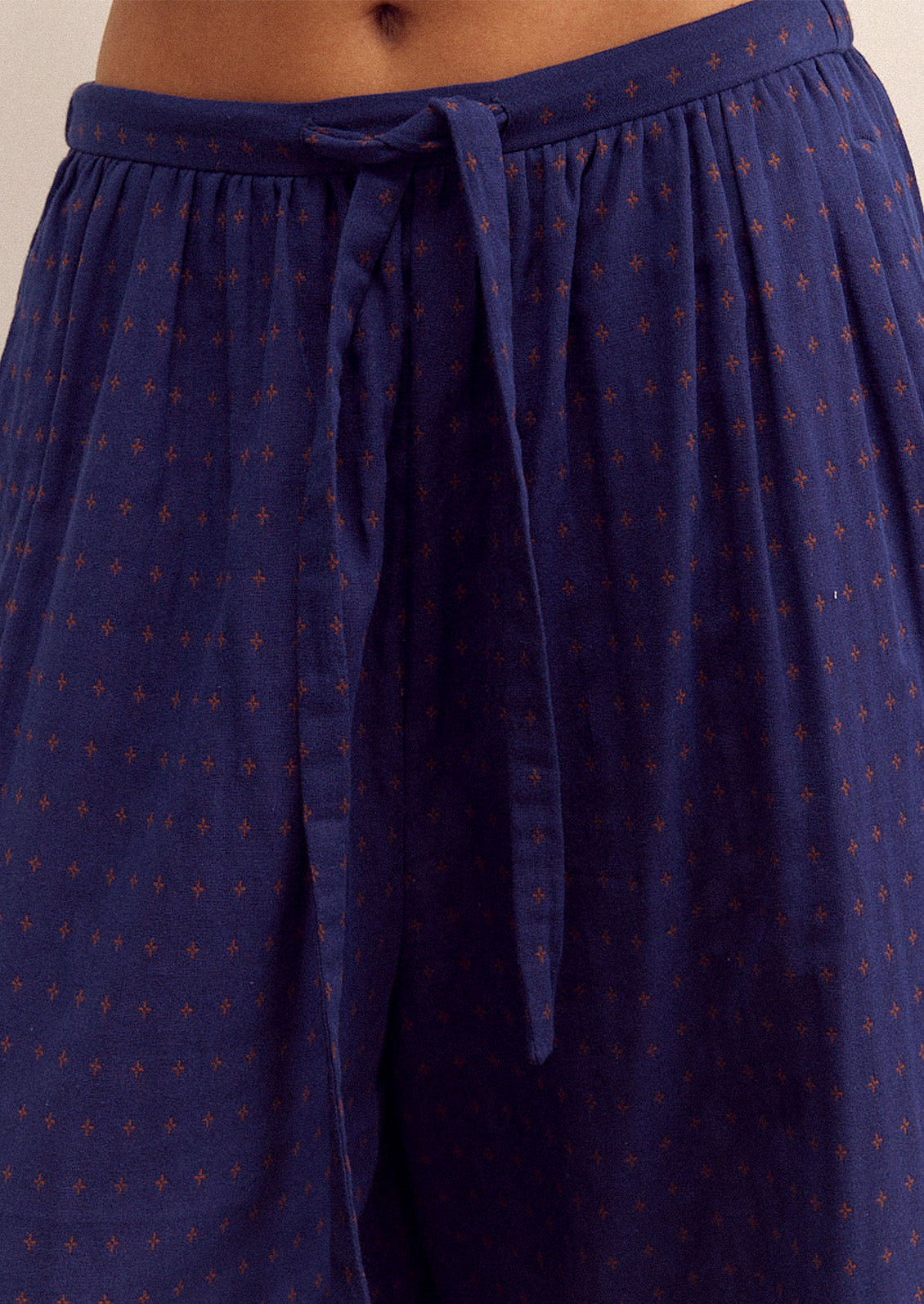 A person wearing a pair of cropped, wide leg pants in navy blue with tiny orange cross pattern.