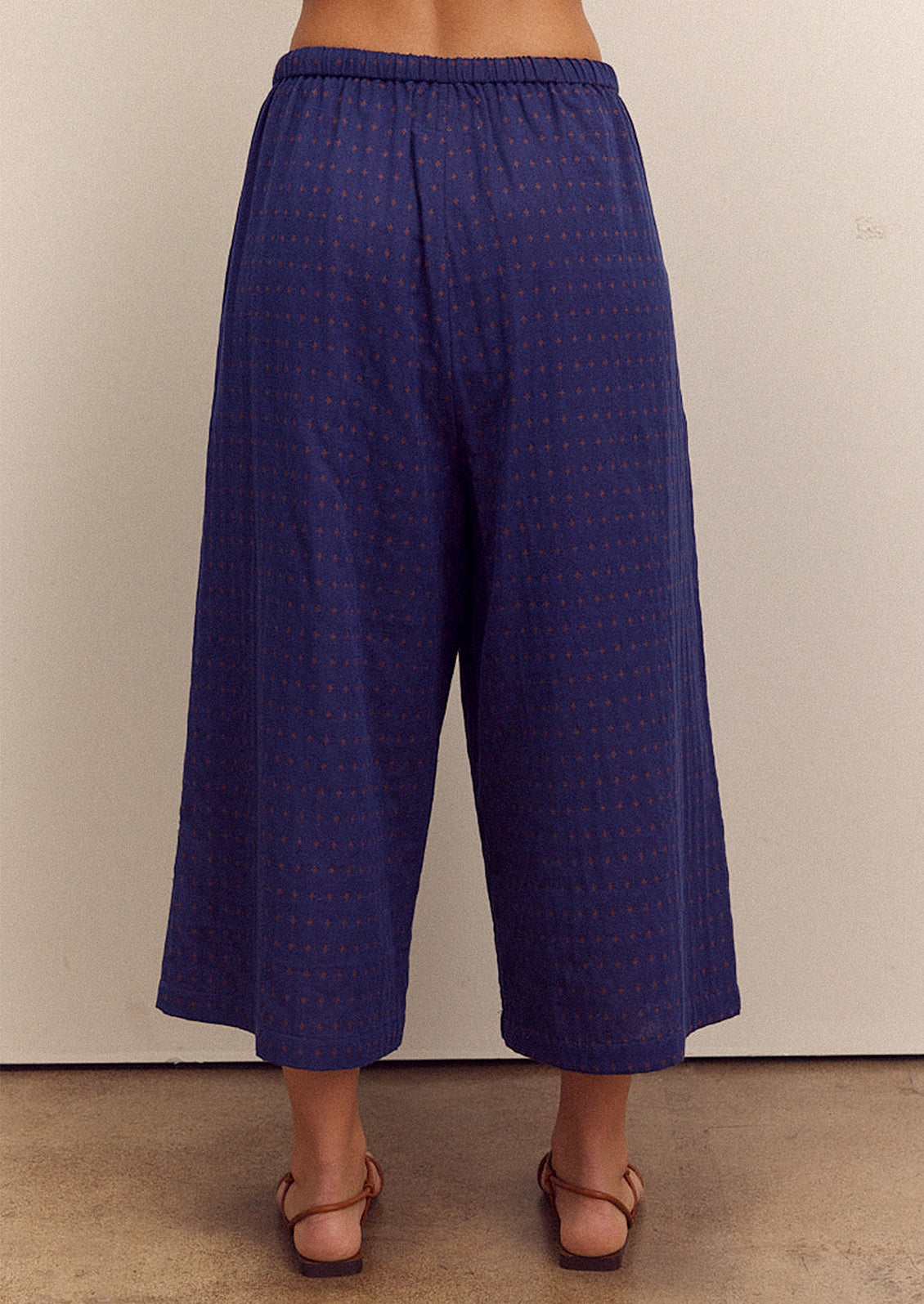 A person wearing a pair of cropped, wide leg pants in navy blue with tiny orange cross pattern.