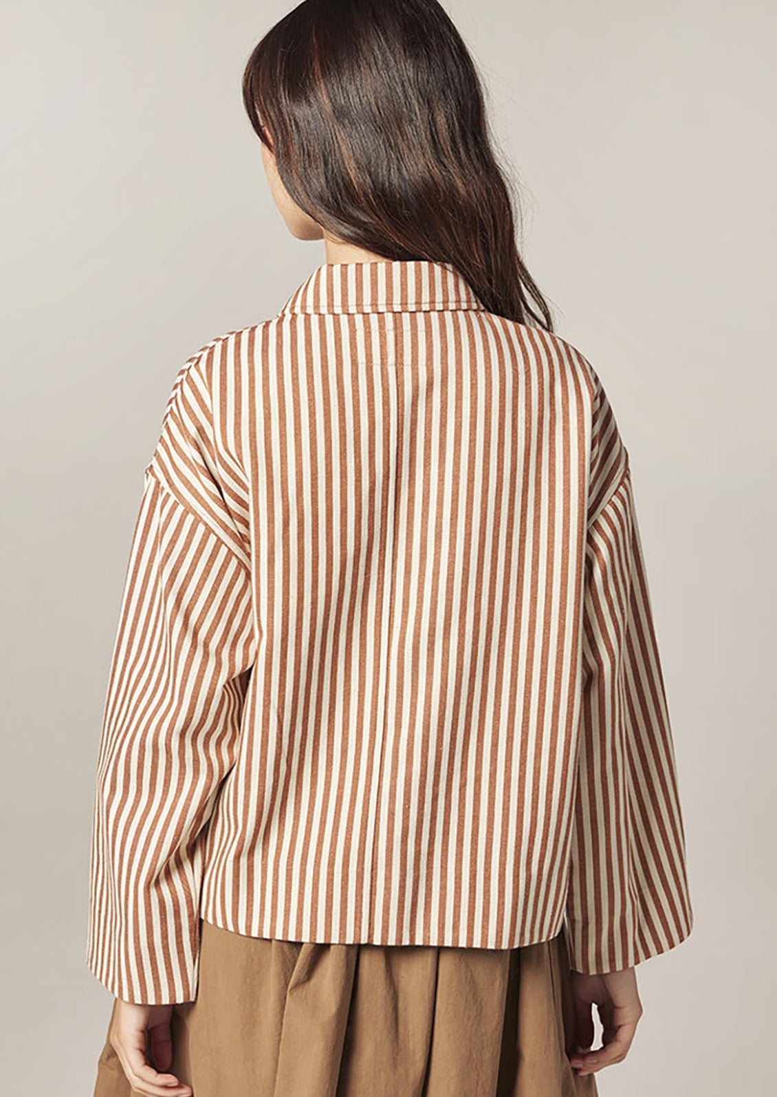 Woman wearing a brown and white striped shirt against a plain background