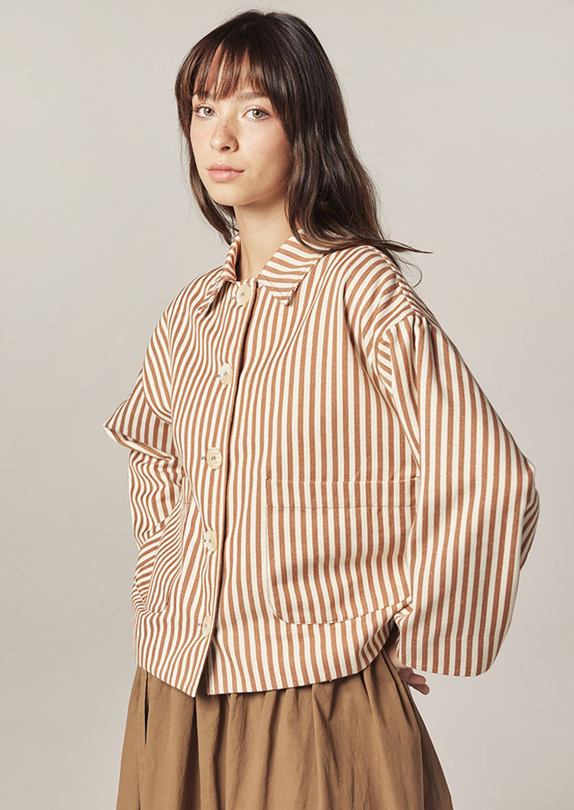 Woman wearing a brown and white striped shirt against a plain background