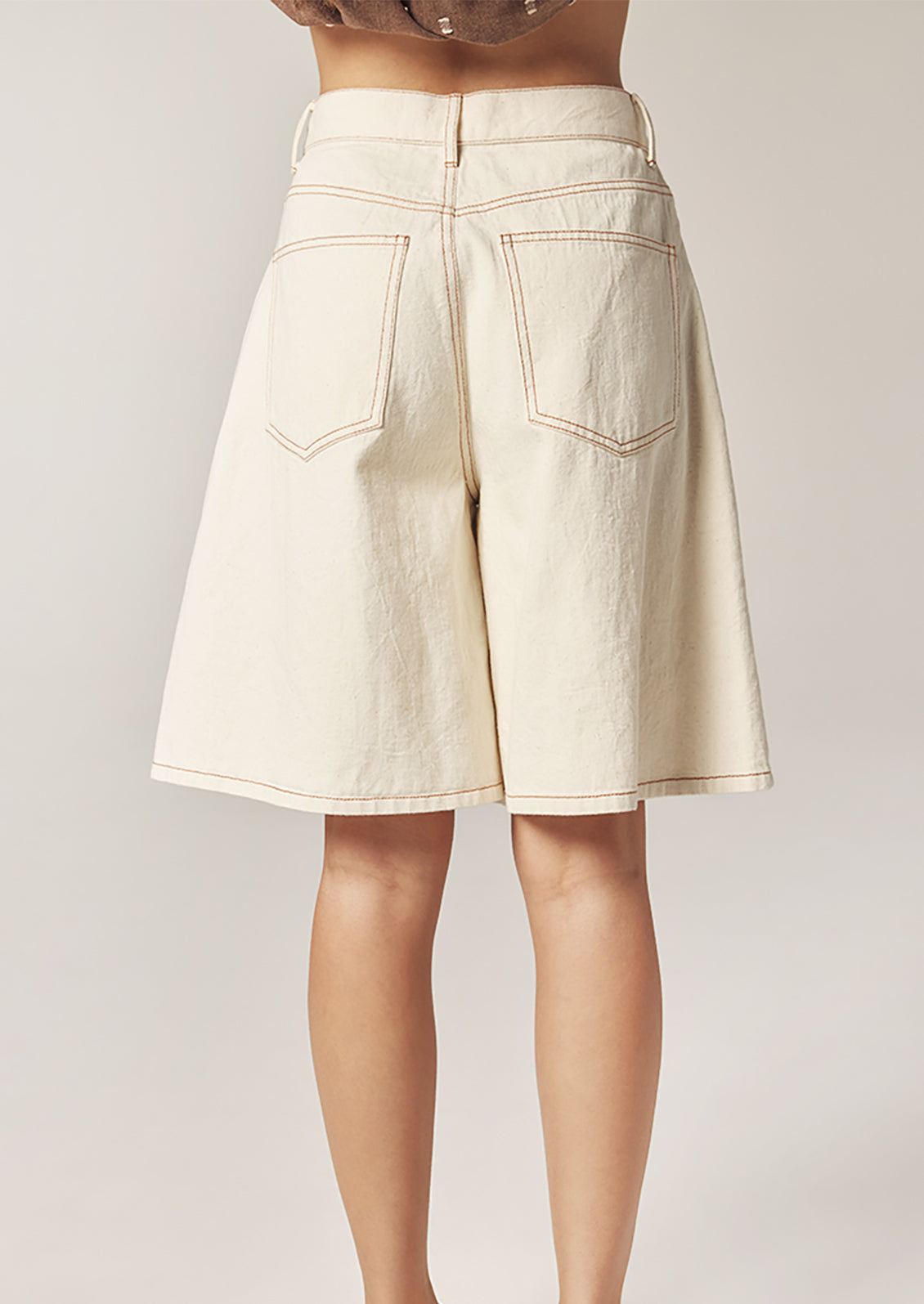 Beige denim shorts worn by a person on a plain background