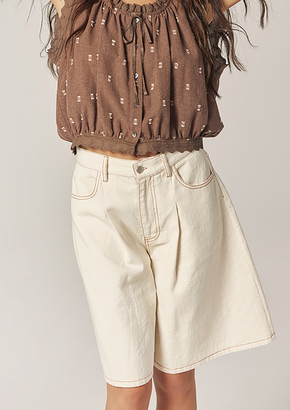 Person wearing a brown patterned top and beige shorts on a plain background