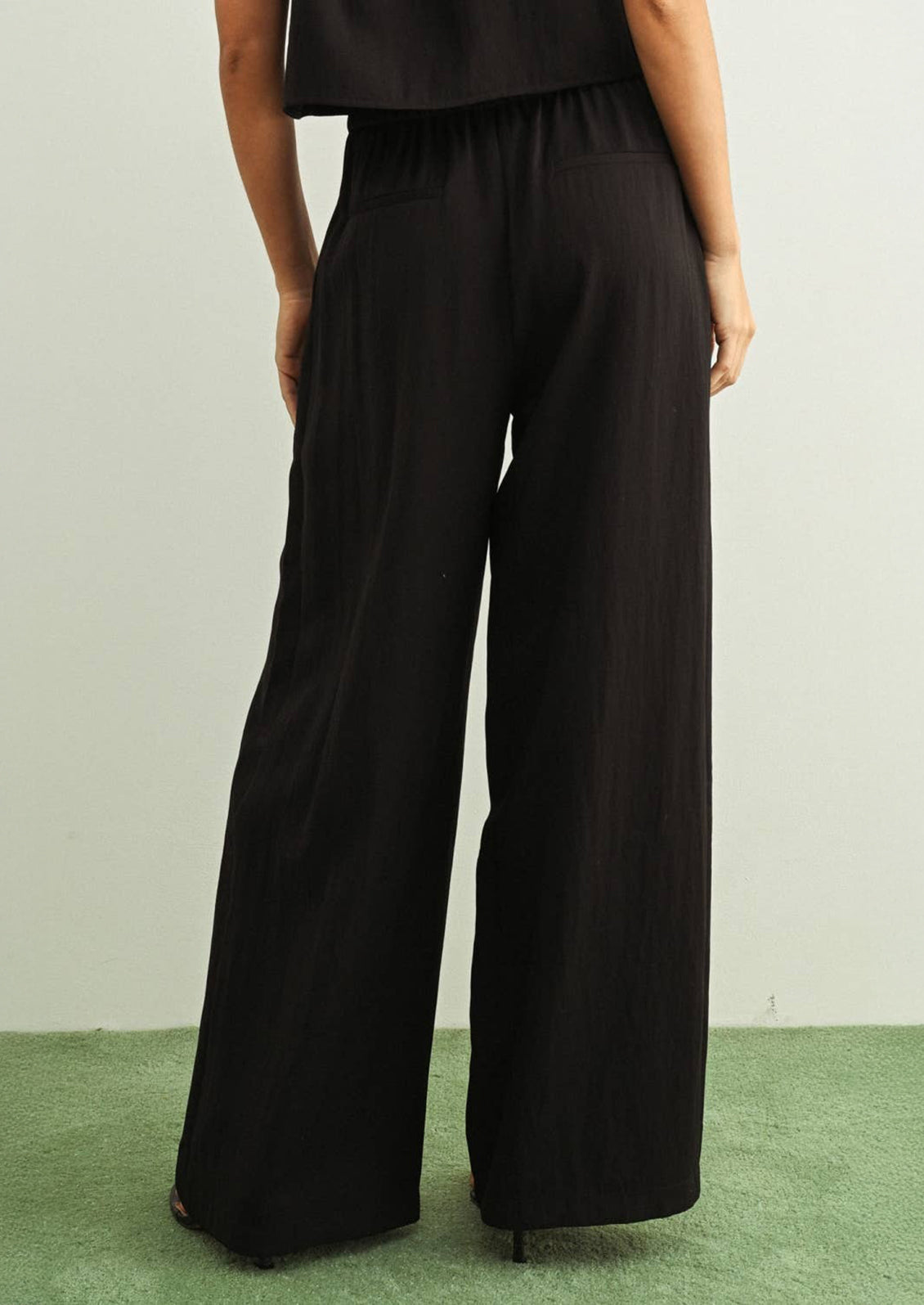 Person wearing black wide-leg pants on a green floor with a neutral wall background