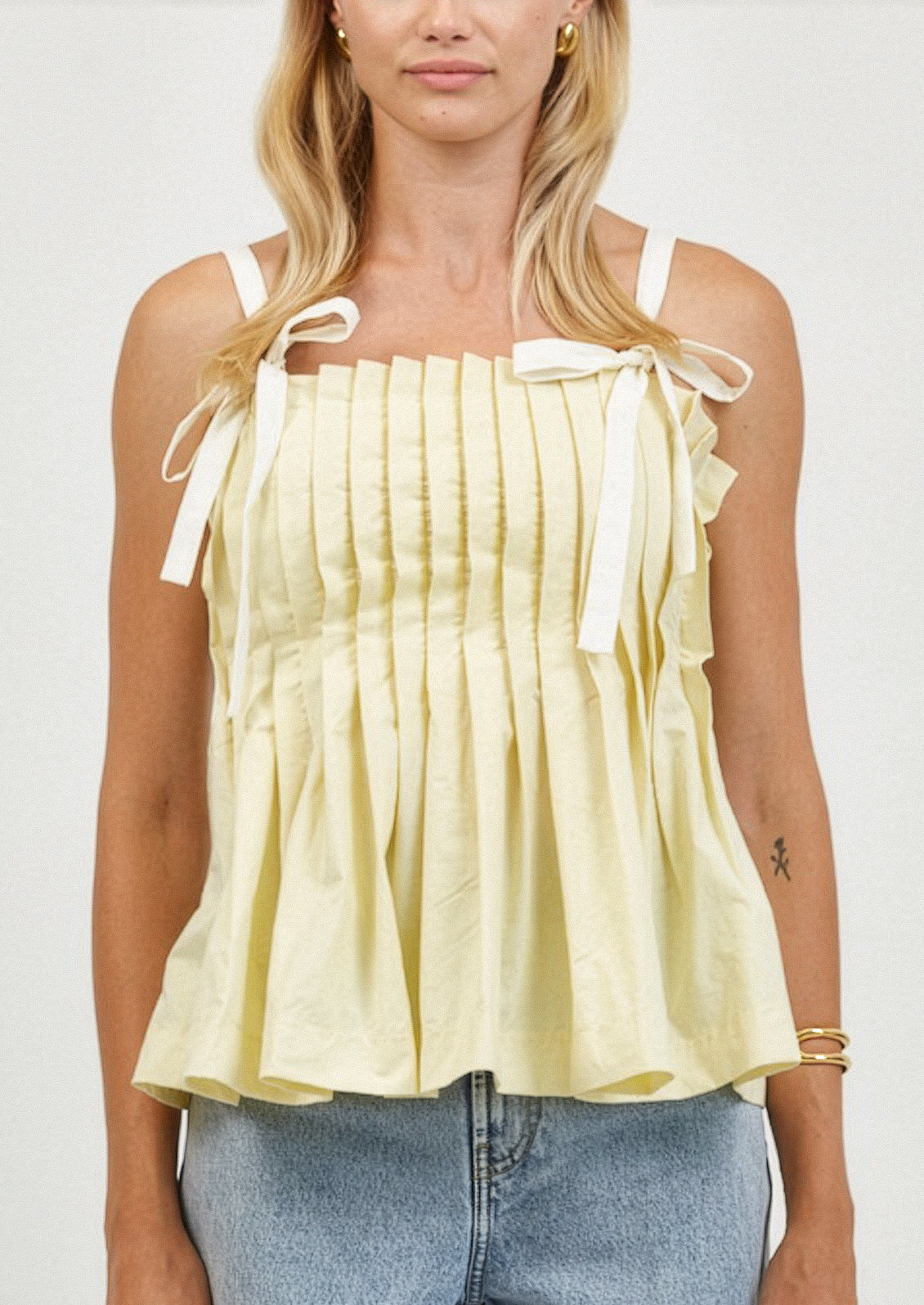 Woman wearing a light yellow top with ribbon straps on a plain background