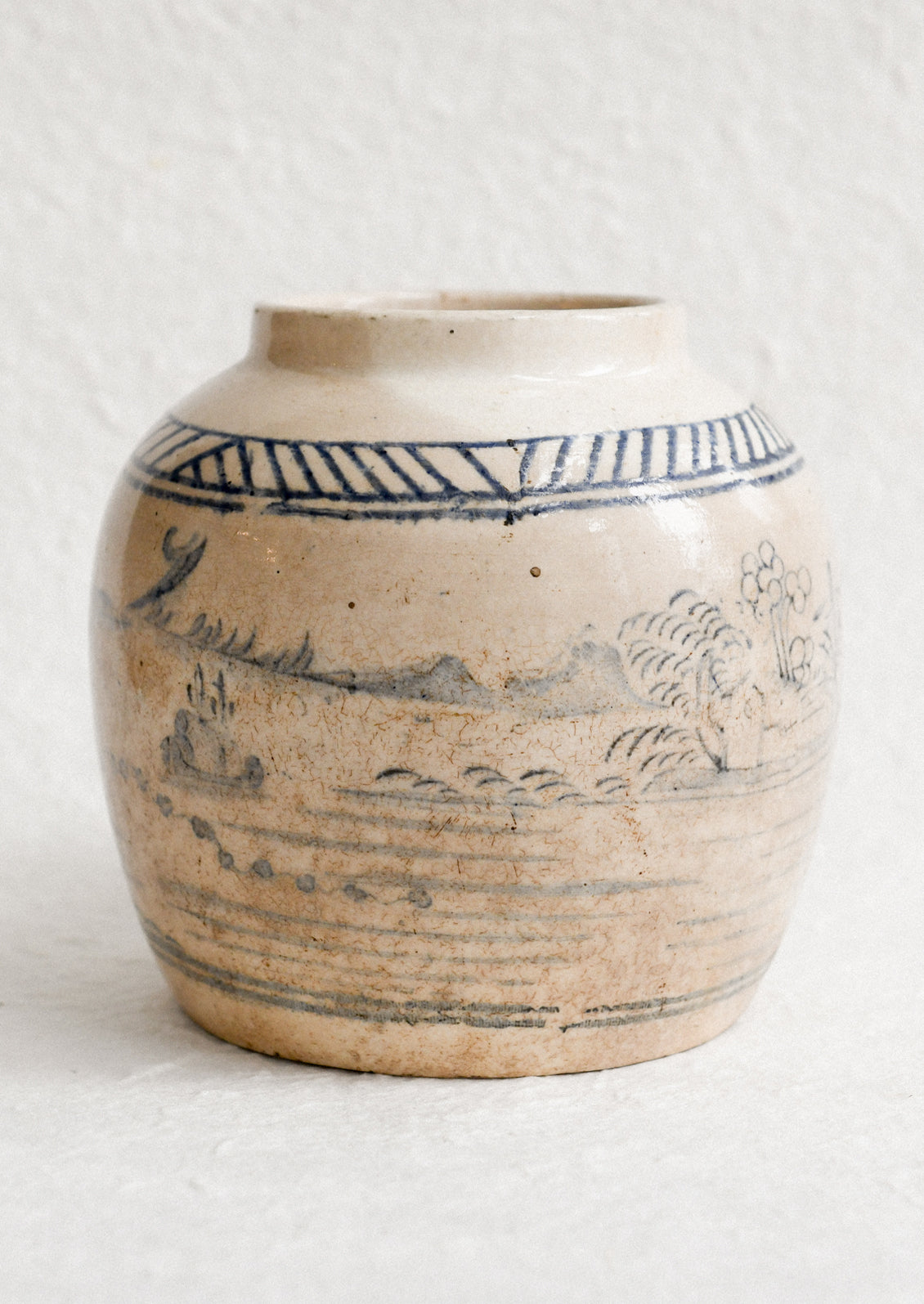 An aged stoneware ginger jar in beige patina with scenic scene in blue.