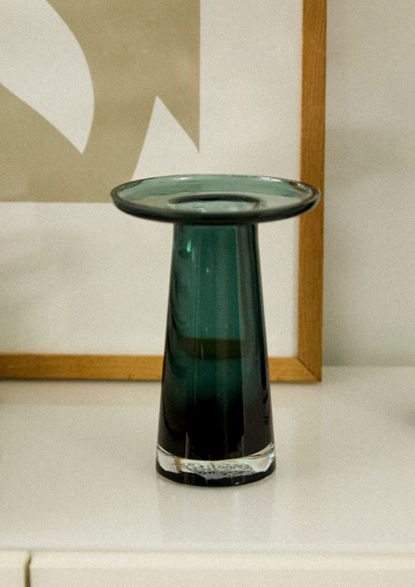 A glass vase in dark teal color, with round, saucer-like top.