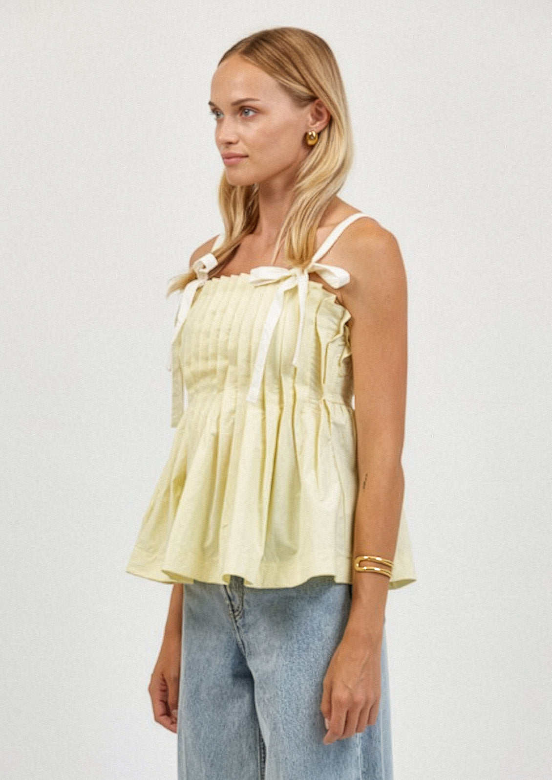 Woman wearing a light yellow top with bow straps and light blue jeans on a white background