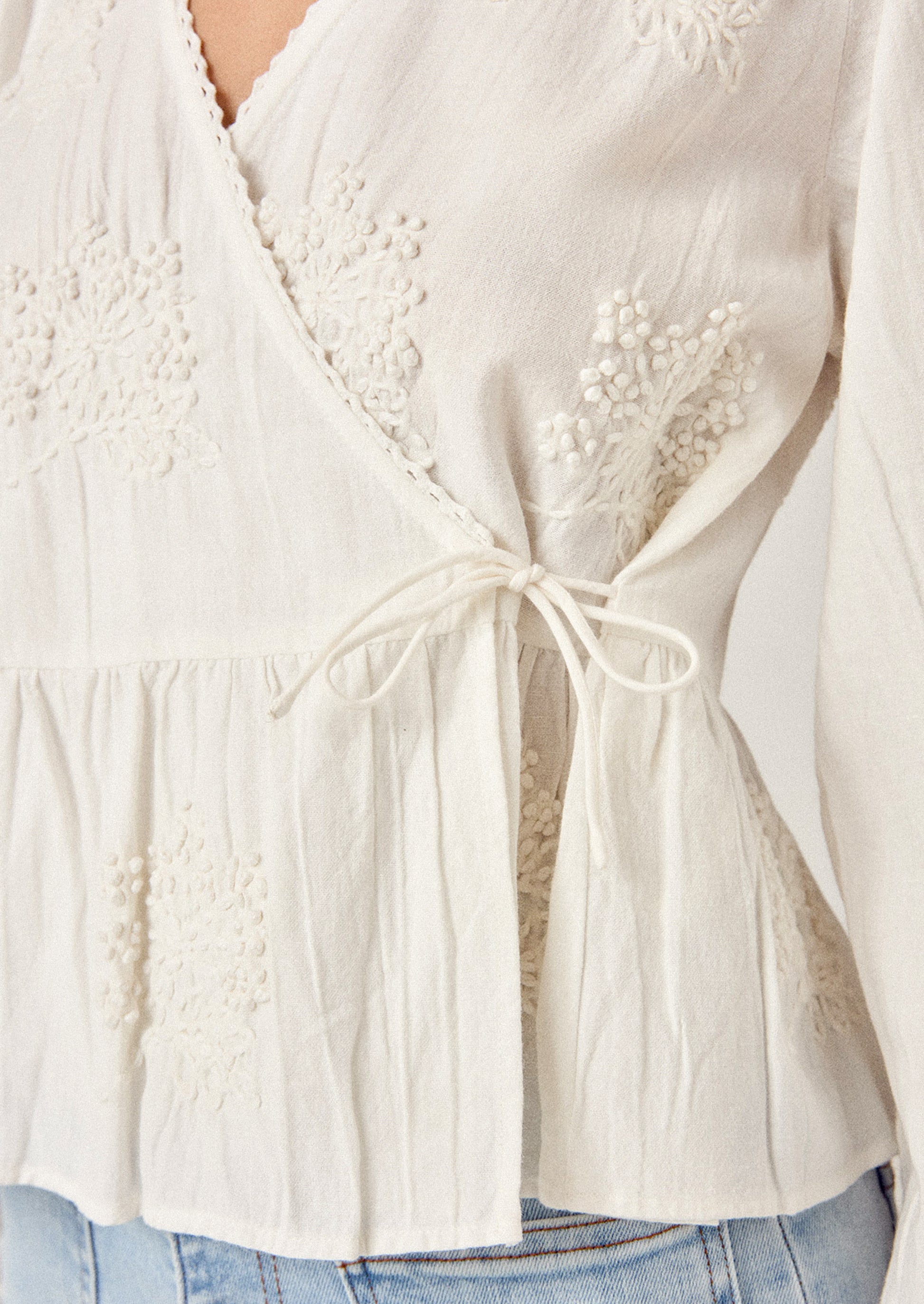 Close-up of a white blouse with lace details and a tie waist.
