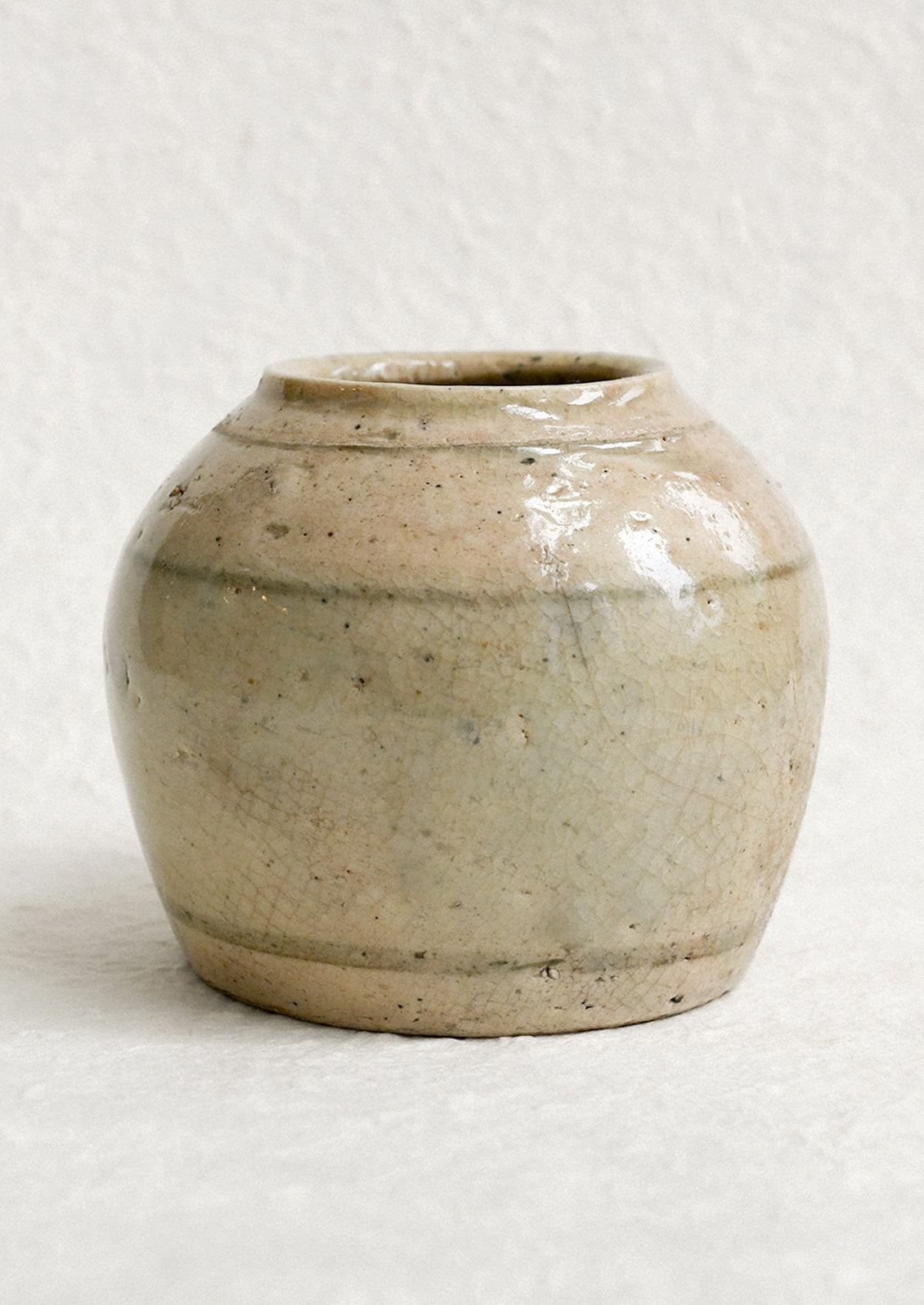 A small ironstone antique jar in greyish brown with heavy patina and soft stripe pattern.