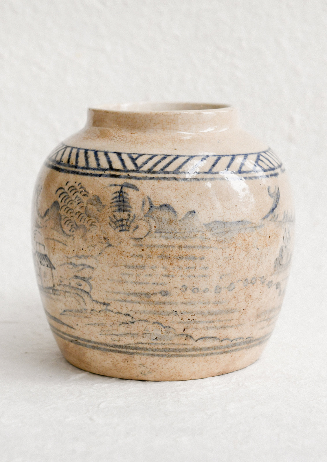 An aged stoneware ginger jar in beige patina with scenic scene in blue.