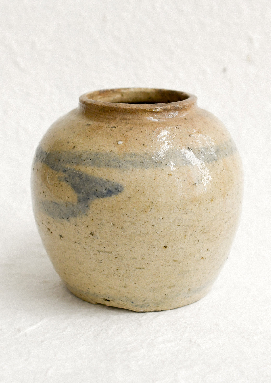 A small antique ginger jar in distressed tan ceramic with pale blue stripes.