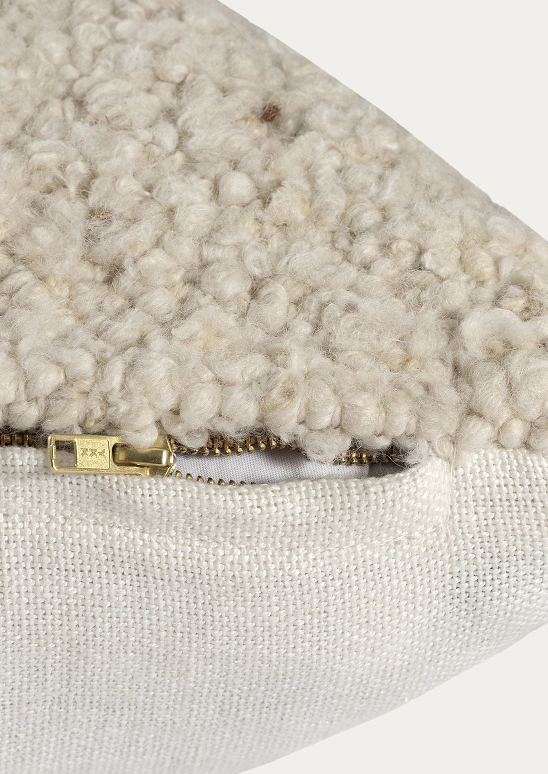 Close-up of a textured cream bouclé fabric meeting a woven off-white fabric, with a small gold zipper pull visible.