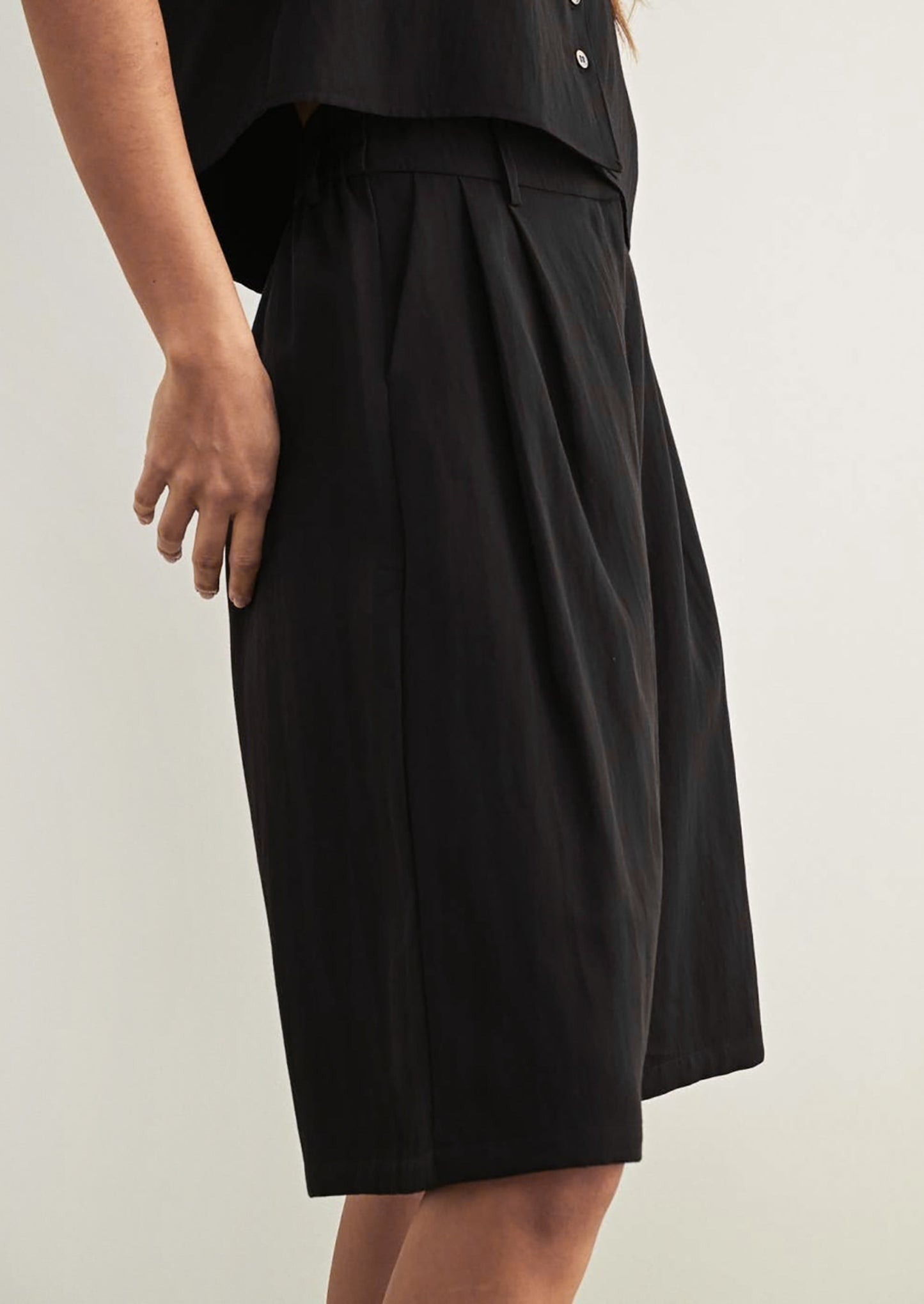 A person wearing a pair of tailored knee-length shorts in black.