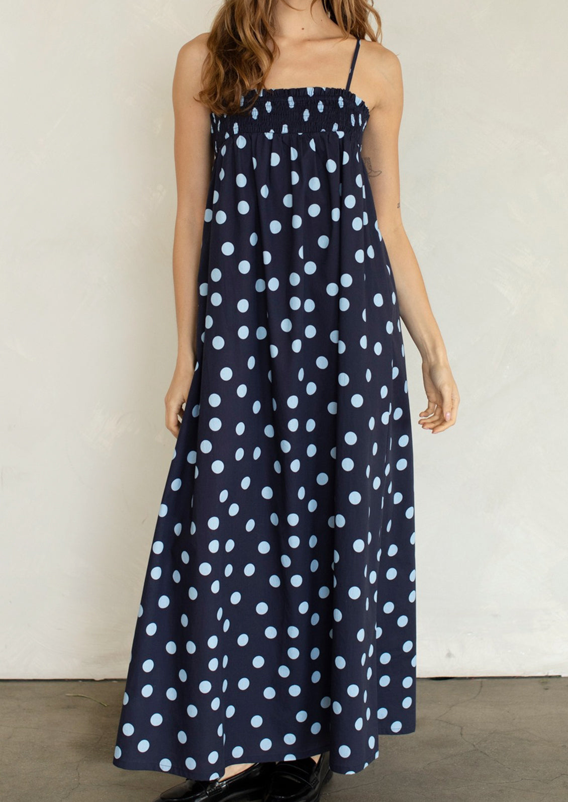 Woman wearing a navy blue dress with white polka dots against a plain background