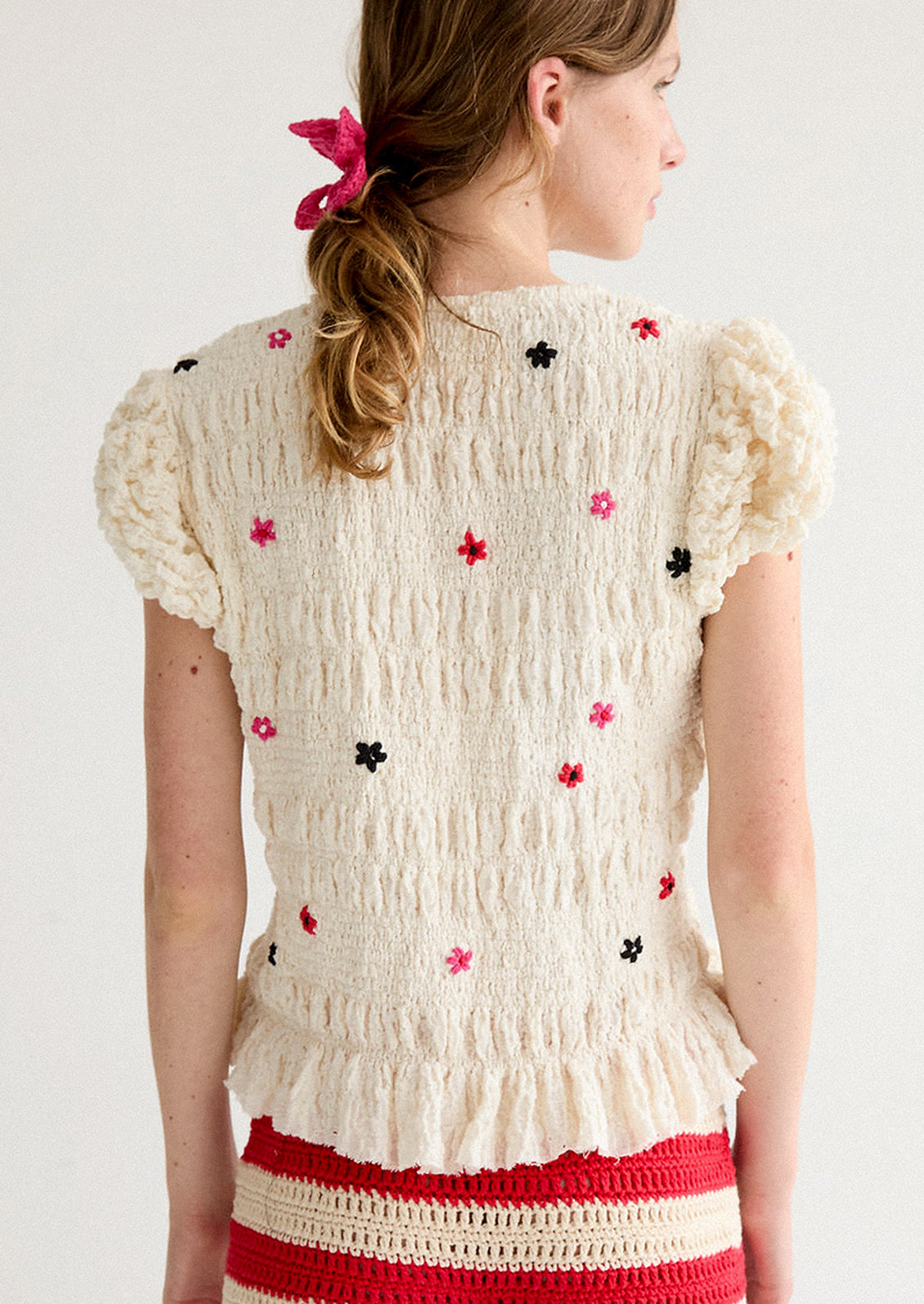A woman wearing a smocked and ruffled cream top with red and pink embroidered flowers throughout.