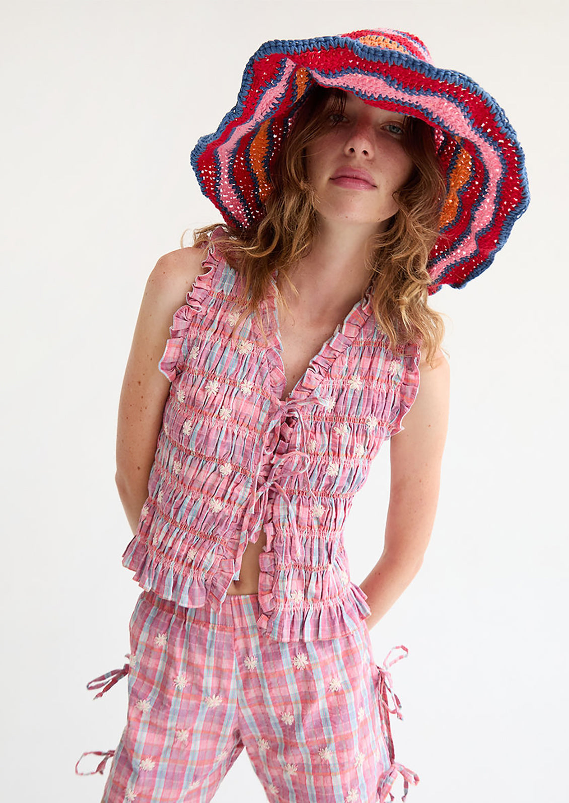 A woman wearing a smocked top in pink and blue, with tie front closure.