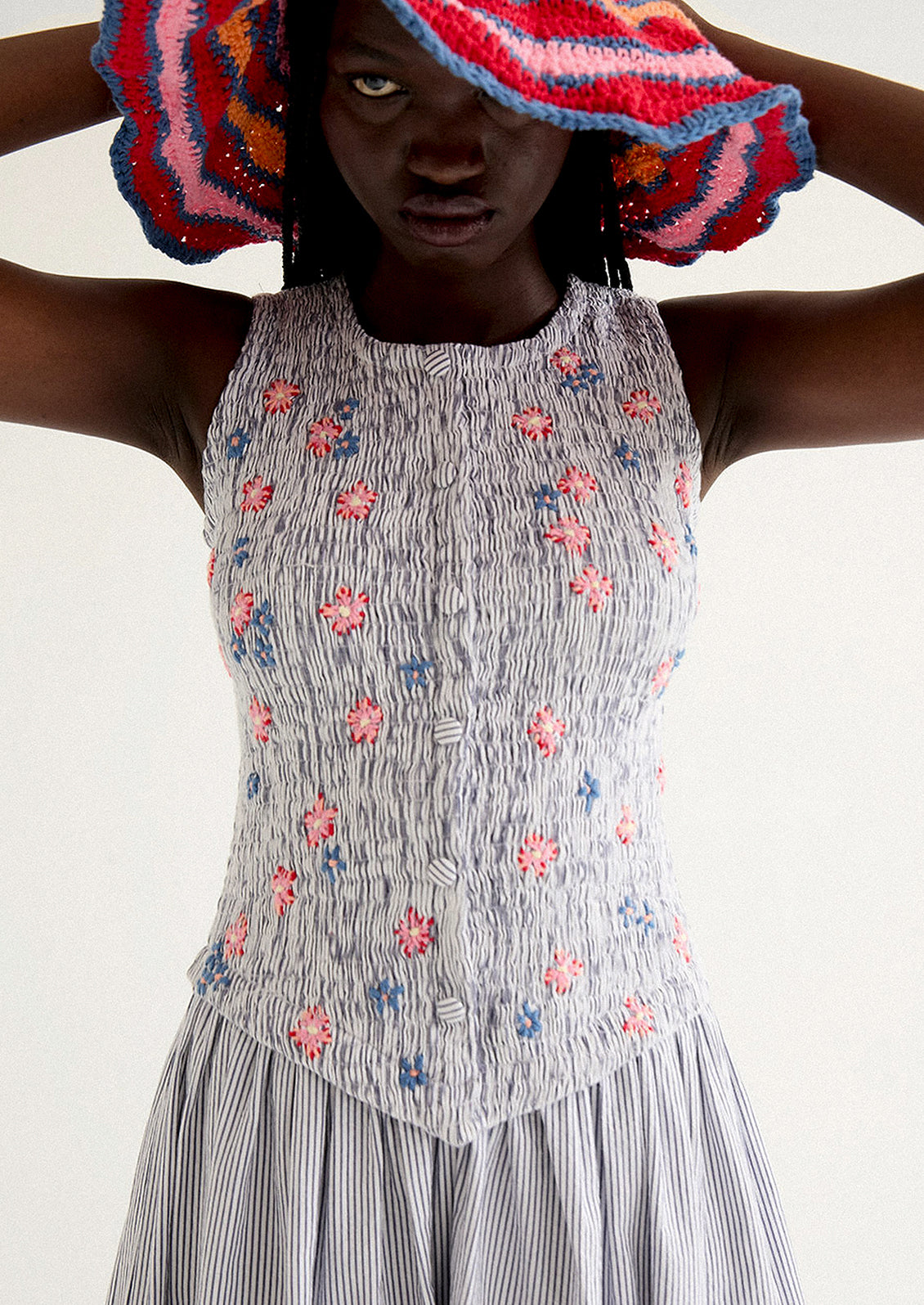 A woman wearing a long striped seersucker dress with smocked bodice featuring floral embroidery detailing.