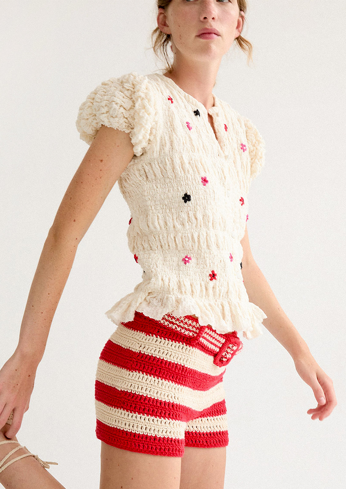 A woman wearing a smocked and ruffled cream top with red and pink embroidered flowers throughout.