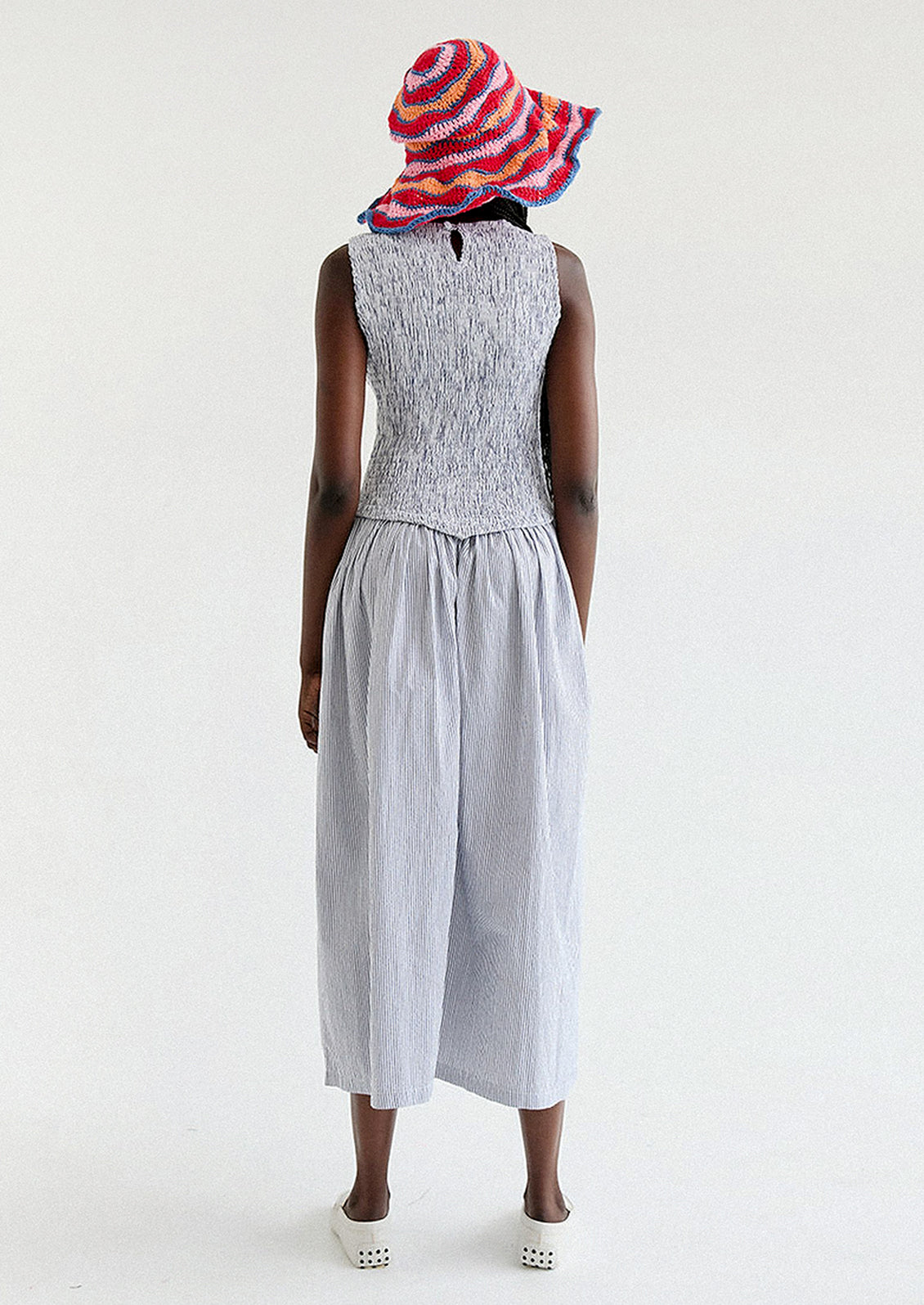 A woman wearing a long striped seersucker dress with smocked bodice featuring floral embroidery detailing.