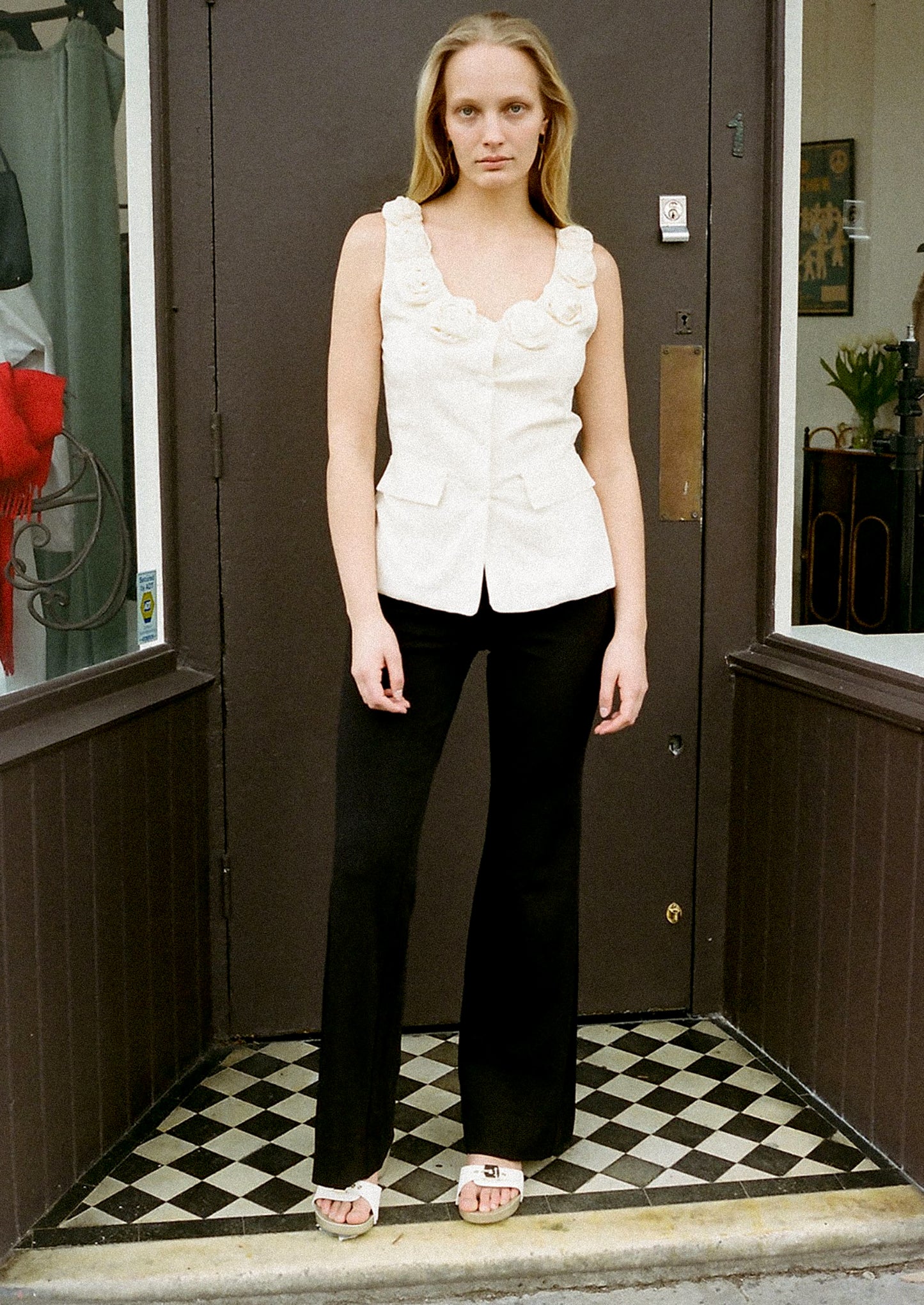 A woman wearing a cream u-neck blouse with dramatic rosette detail along neckline.