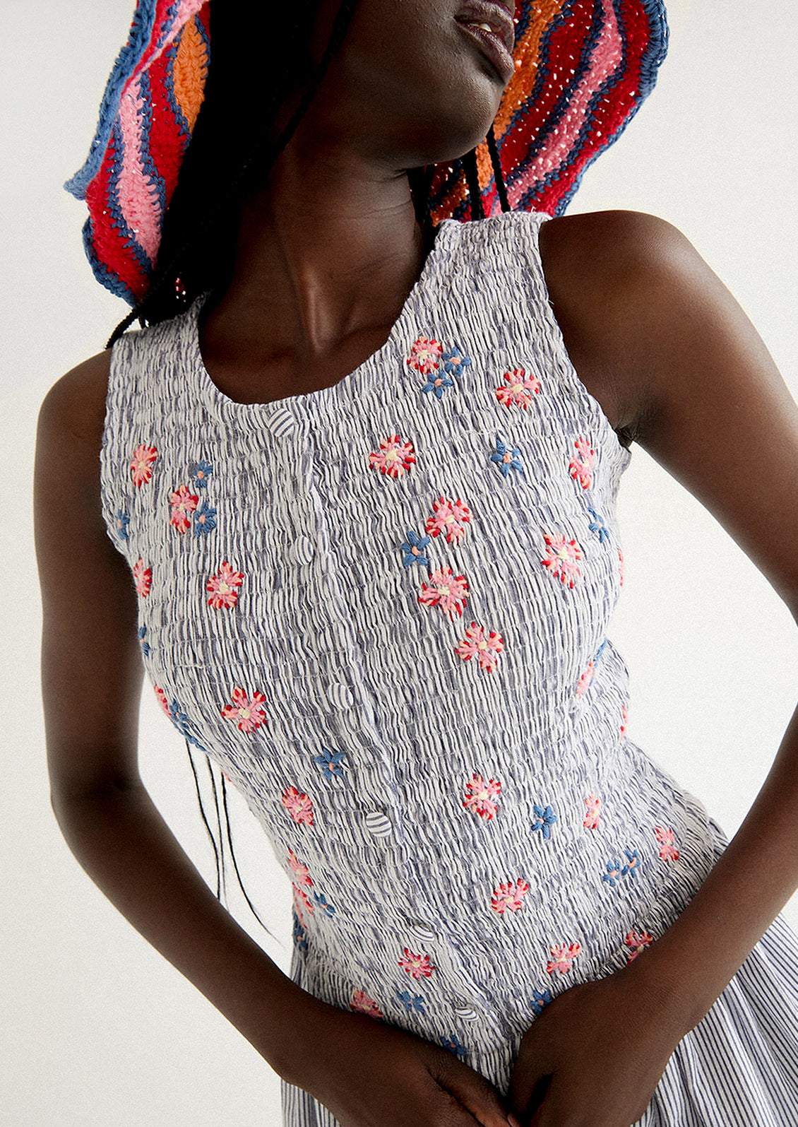 A woman wearing a long striped seersucker dress with smocked bodice featuring floral embroidery detailing.