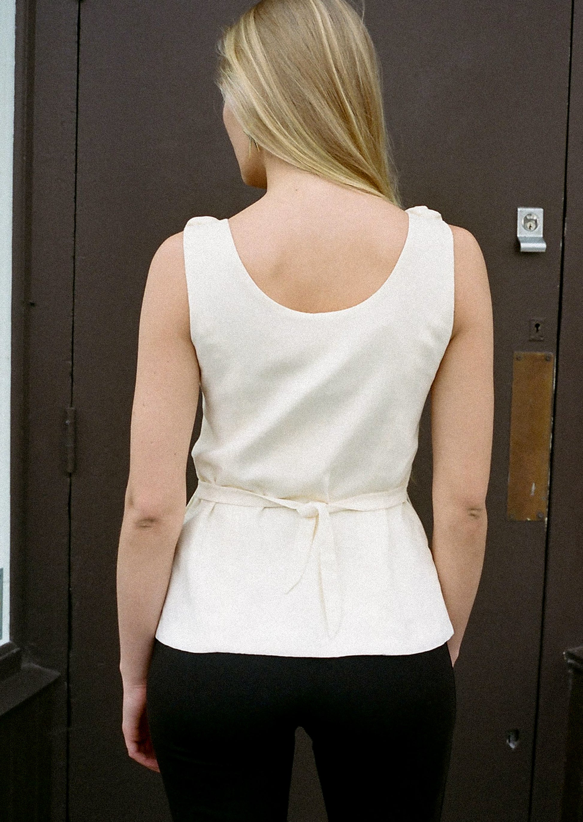 A woman wearing a cream u-neck blouse with dramatic rosette detail along neckline.