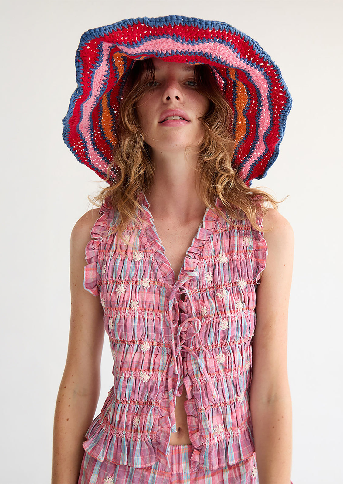 A woman wearing a smocked top in pink and blue, with tie front closure.