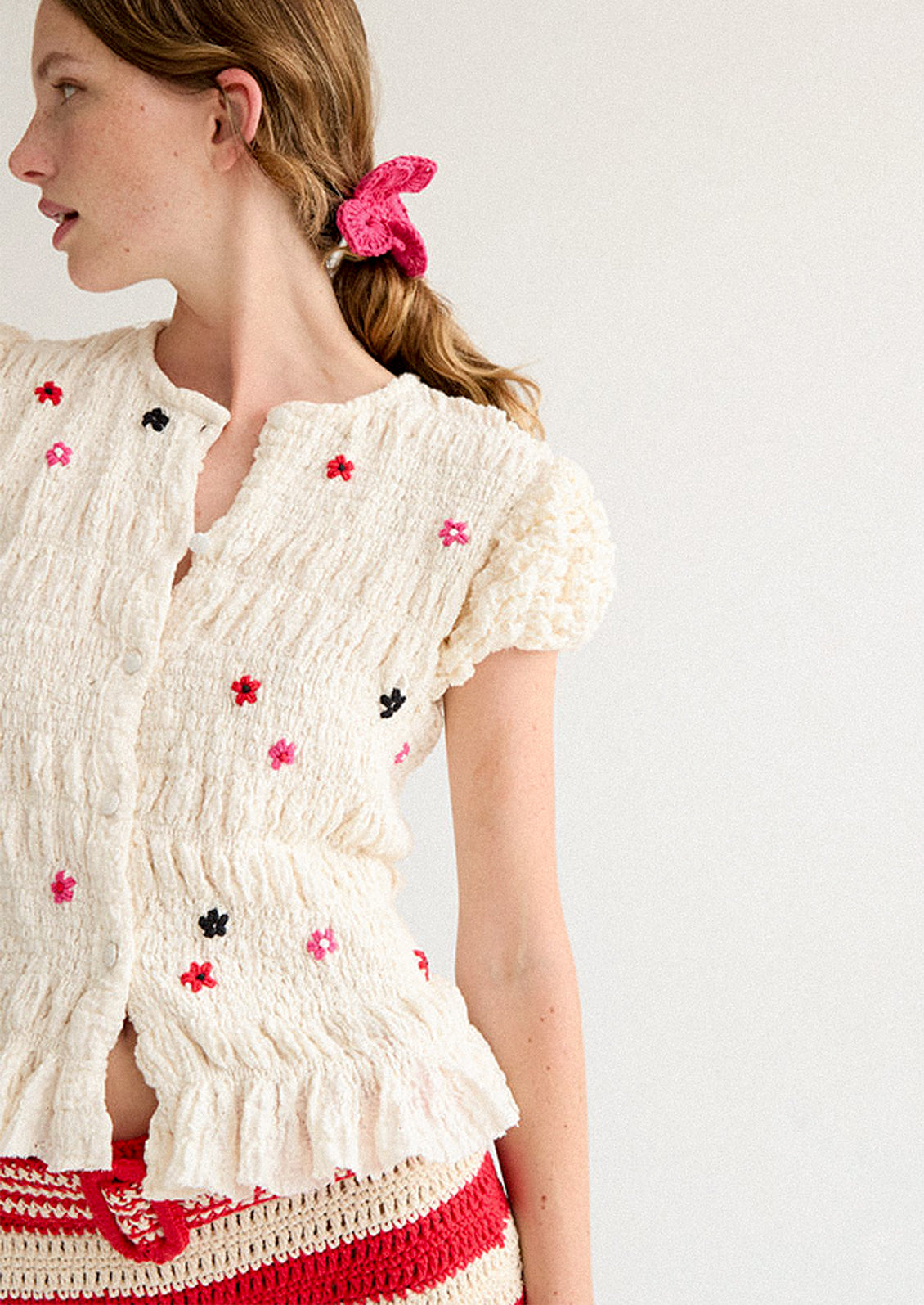 A woman wearing a smocked and ruffled cream top with red and pink embroidered flowers throughout.