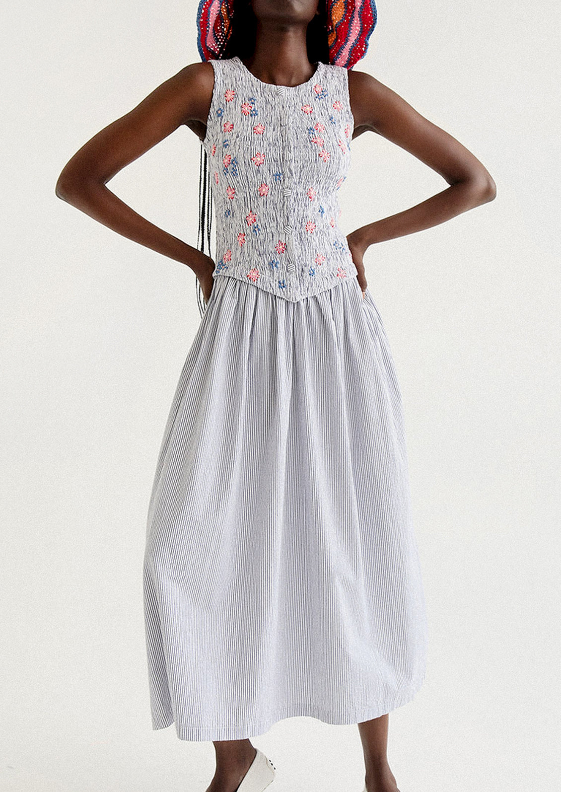 A woman wearing a long striped seersucker dress with smocked bodice featuring floral embroidery detailing.