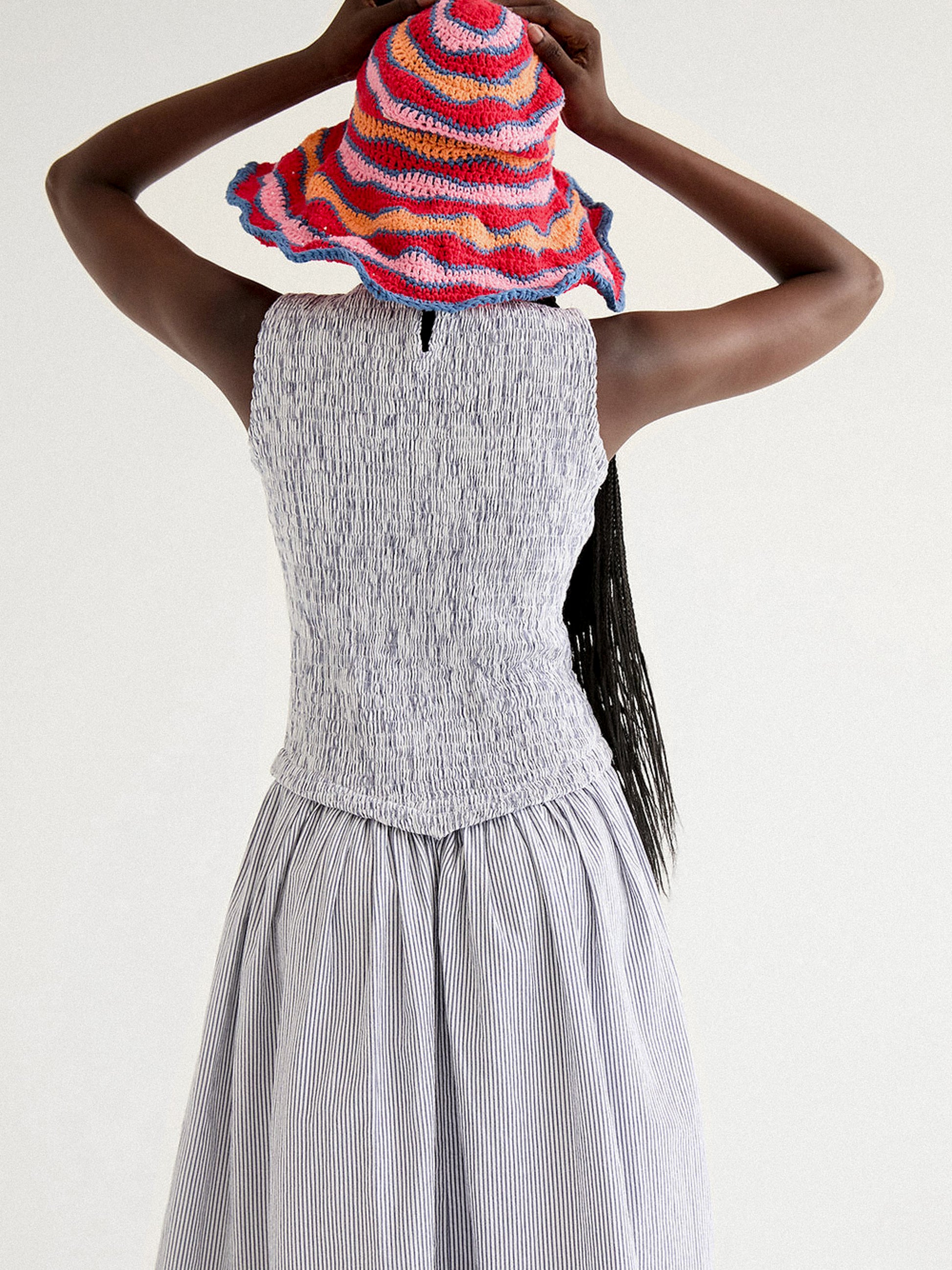 A woman wearing a long striped seersucker dress with smocked bodice featuring floral embroidery detailing.