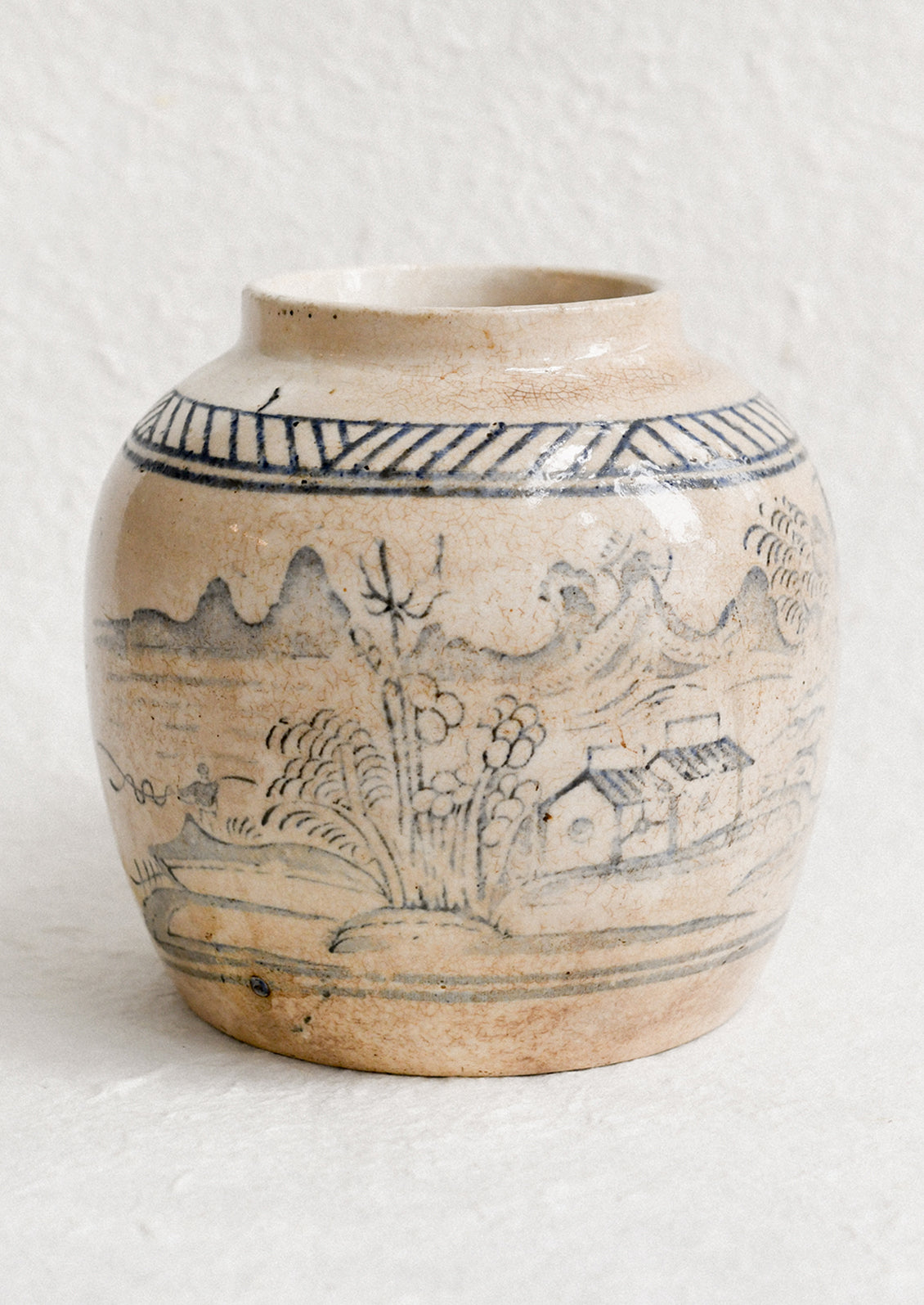 An aged stoneware ginger jar in beige patina with scenic scene in blue.