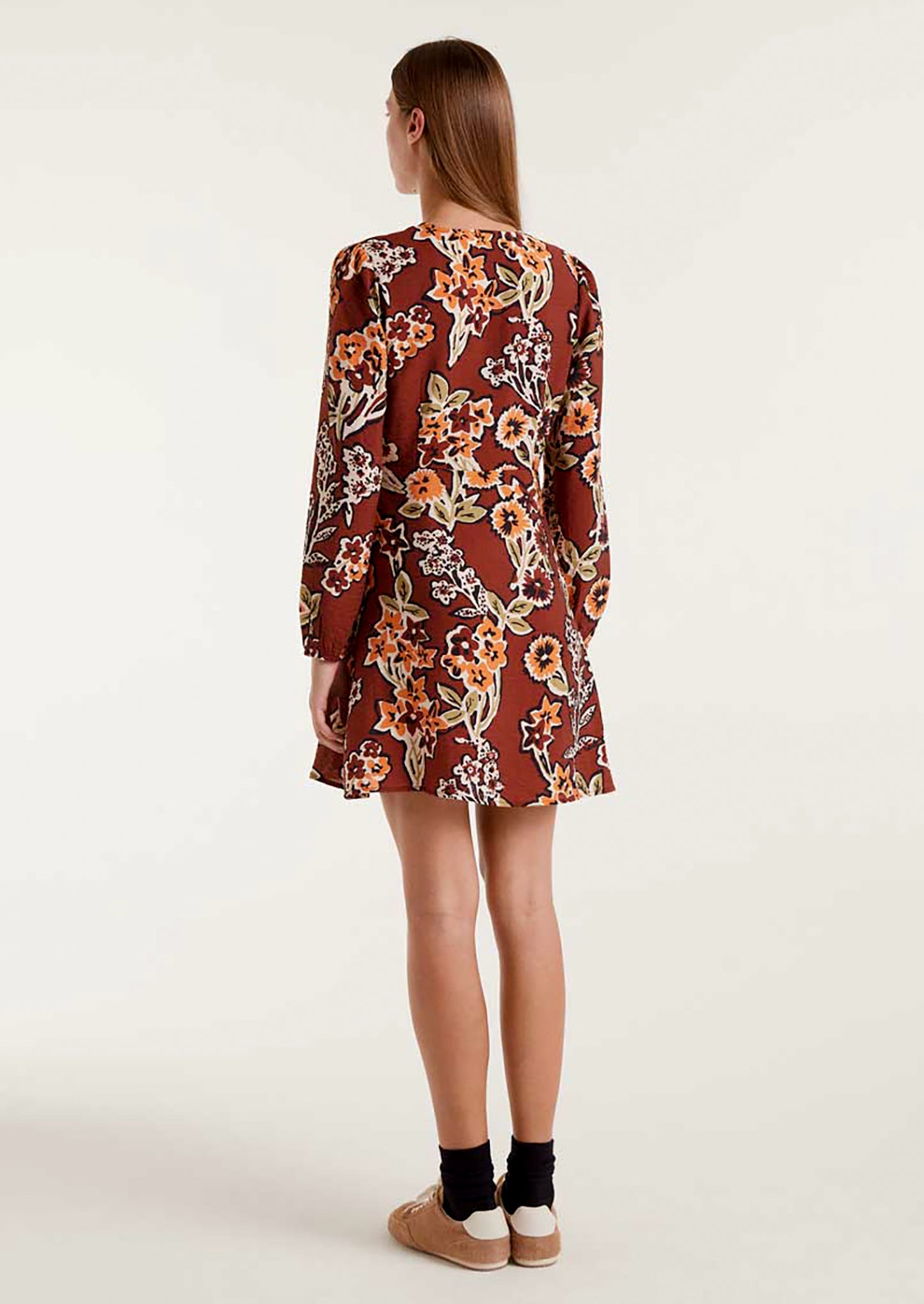 A woman wearing a brown mini long sleeve dress with orange and green floral pattern.