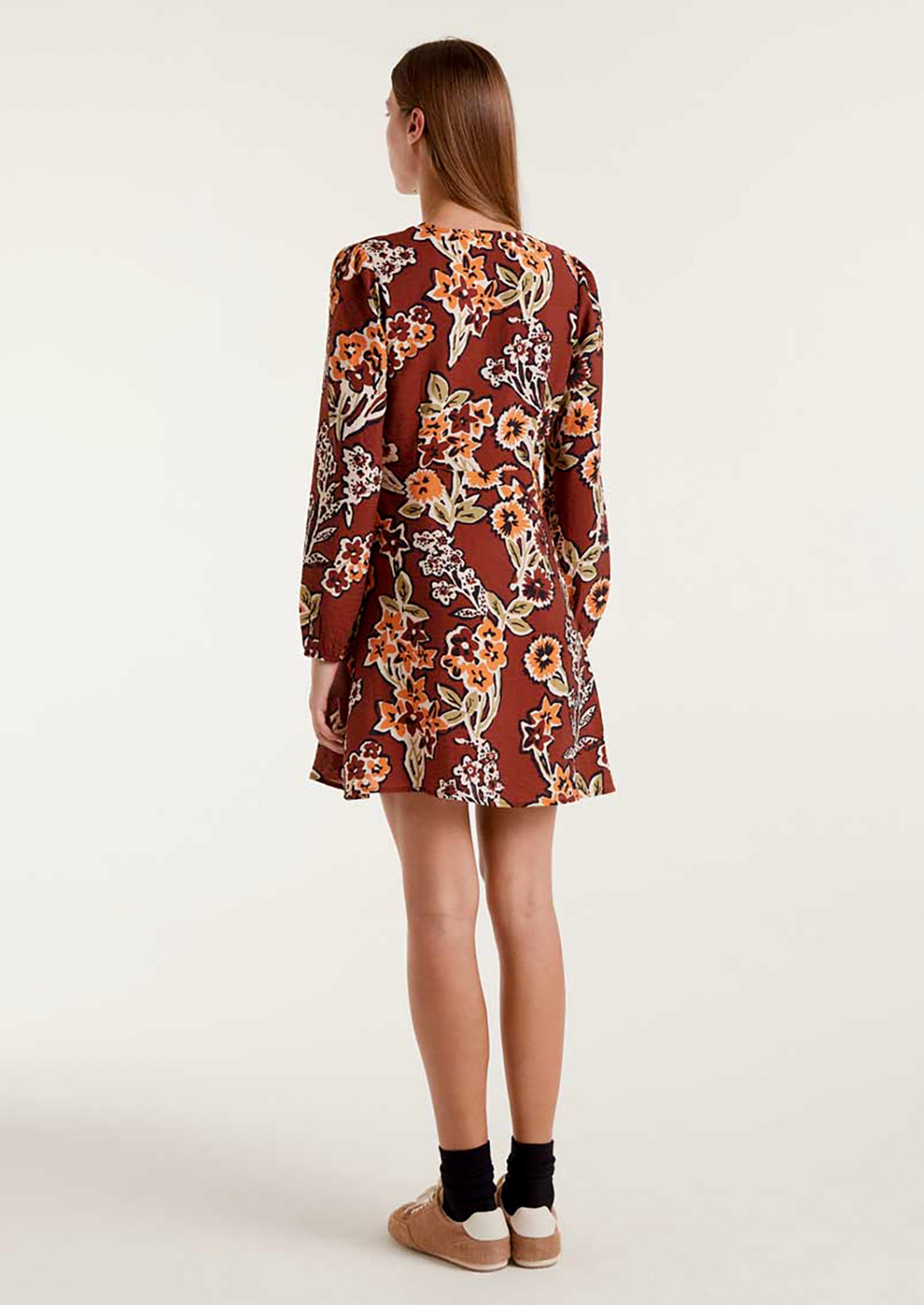 A woman wearing a brown mini long sleeve dress with orange and green floral pattern.