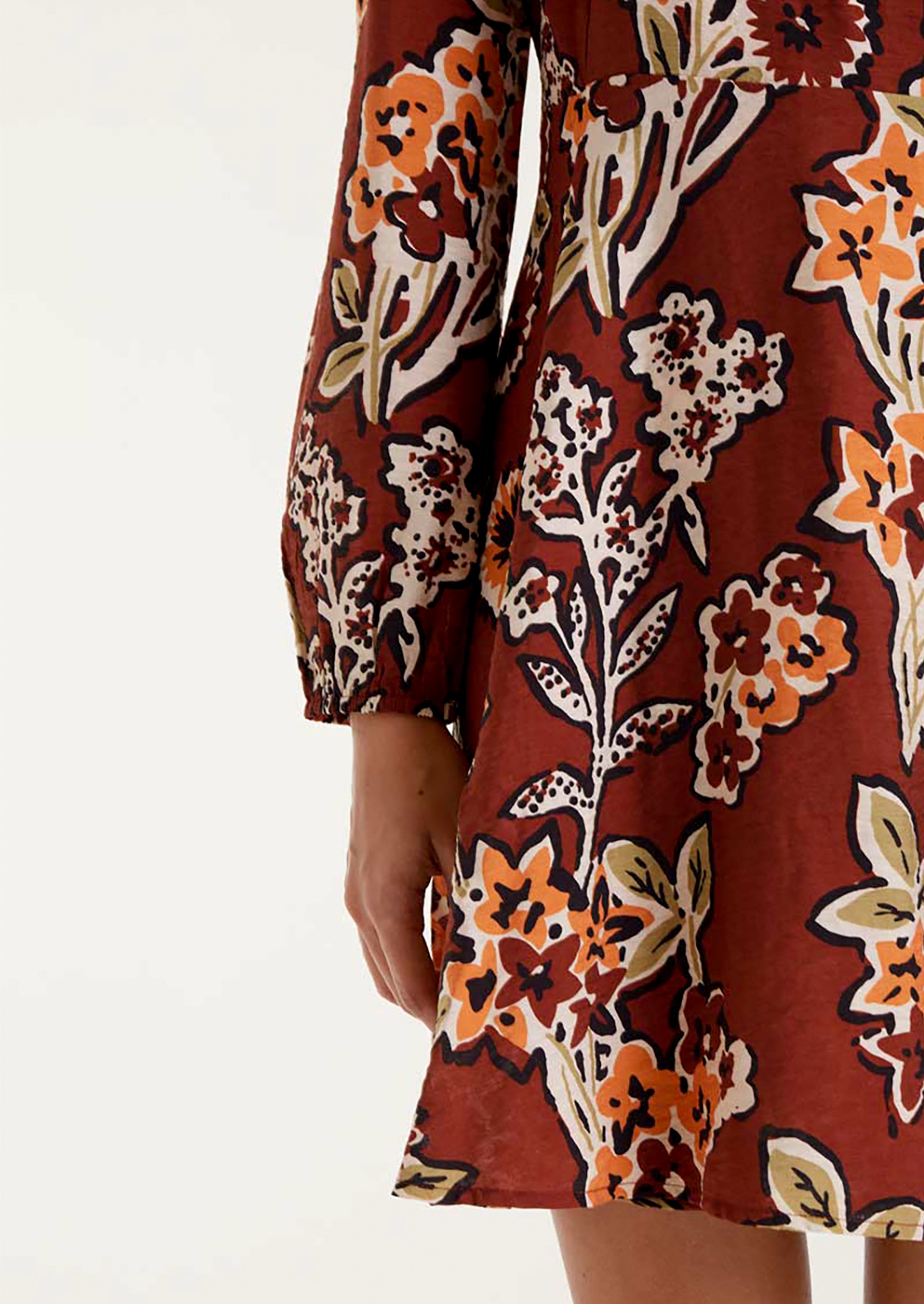 A woman wearing a brown mini long sleeve dress with orange and green floral pattern.