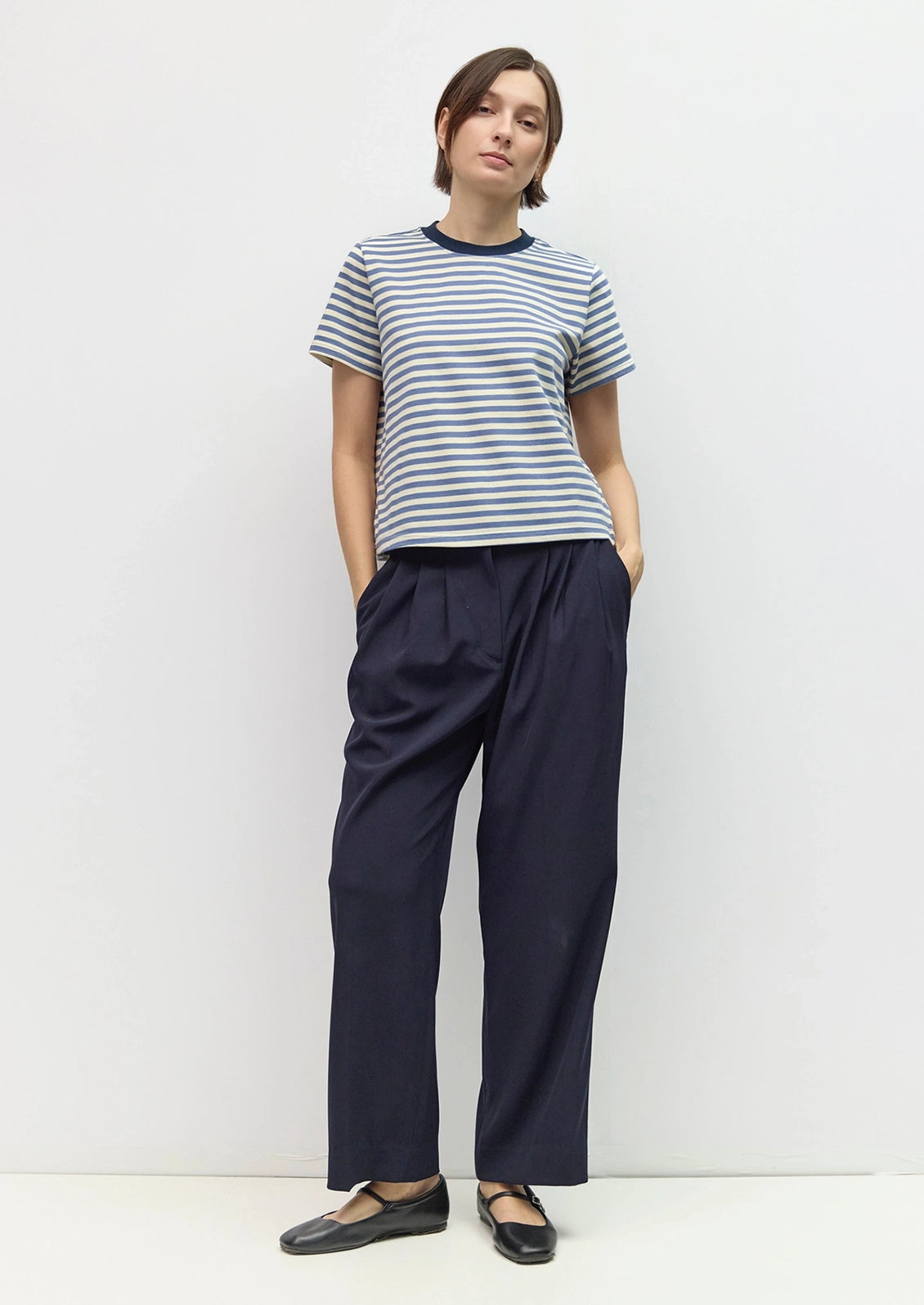 A person wearing a short-sleeve crew-neck striped T-shirt with horizontal navy and off-white stripes.