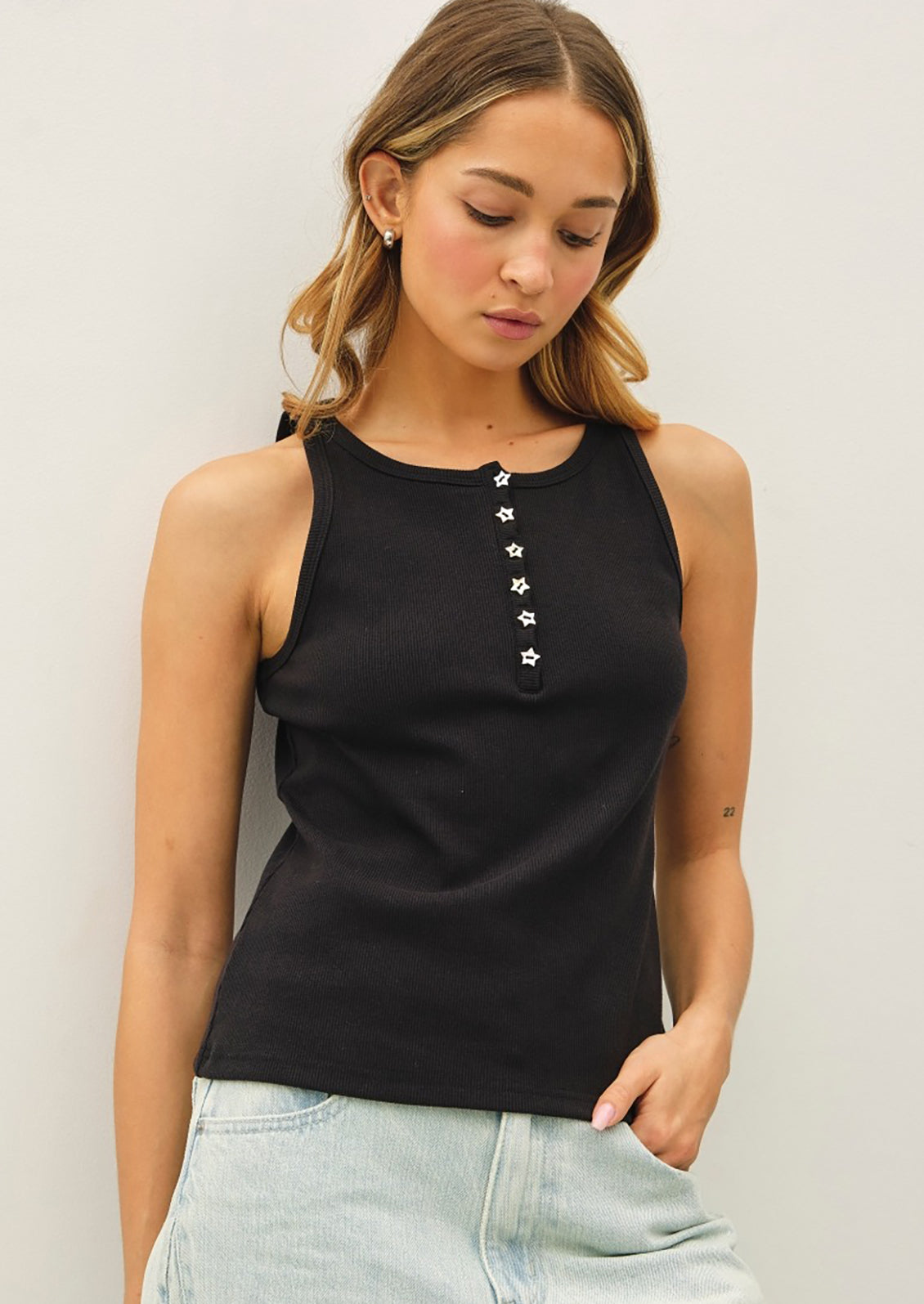 A person wearing a black tank top with star-shaped buttons.