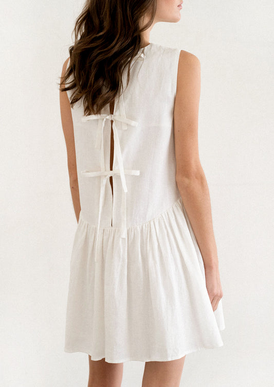 A person wearing a white mini dress with dropwaist and tieback detail.