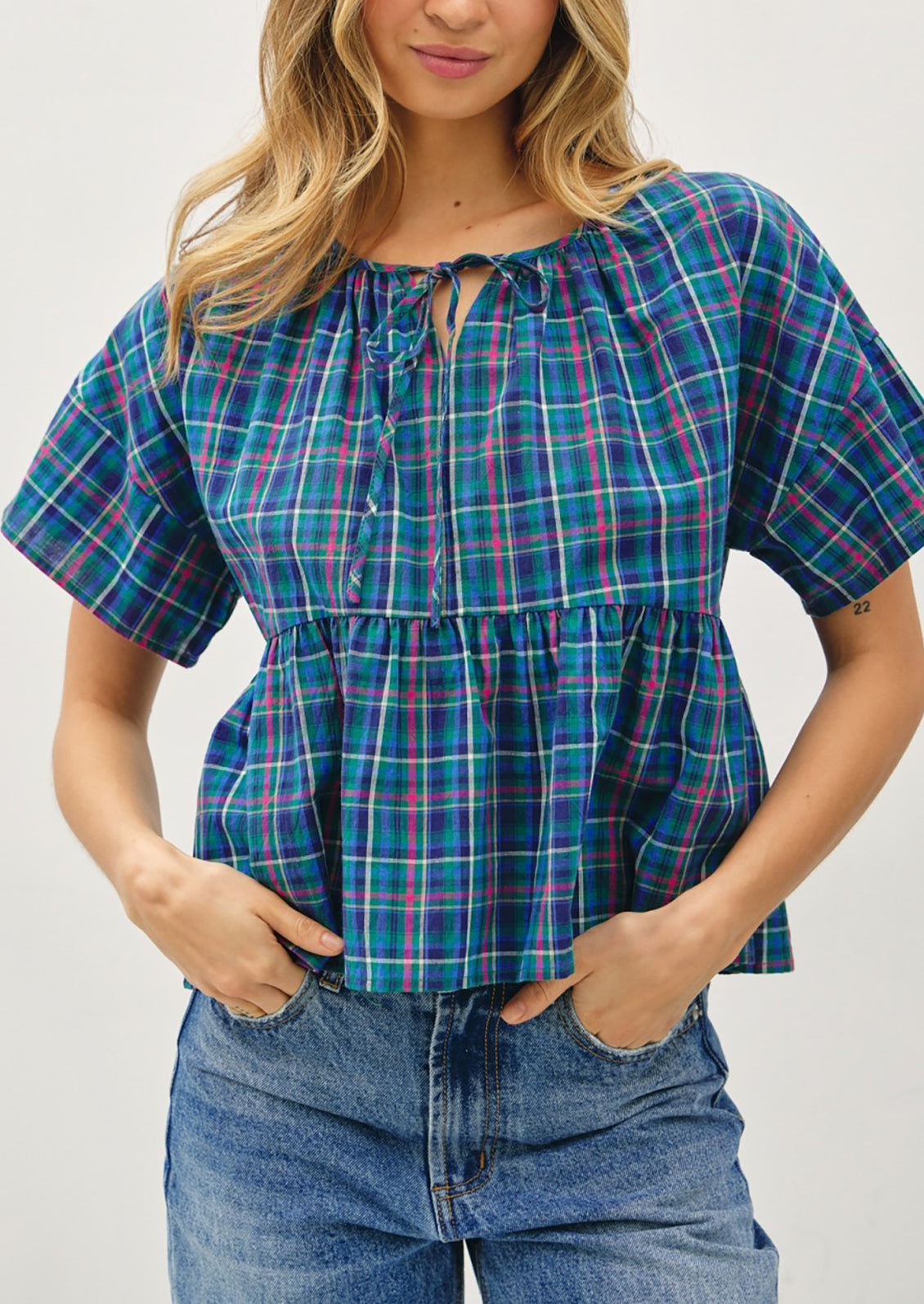 Woman wearing a blue plaid top and jeans against a white background