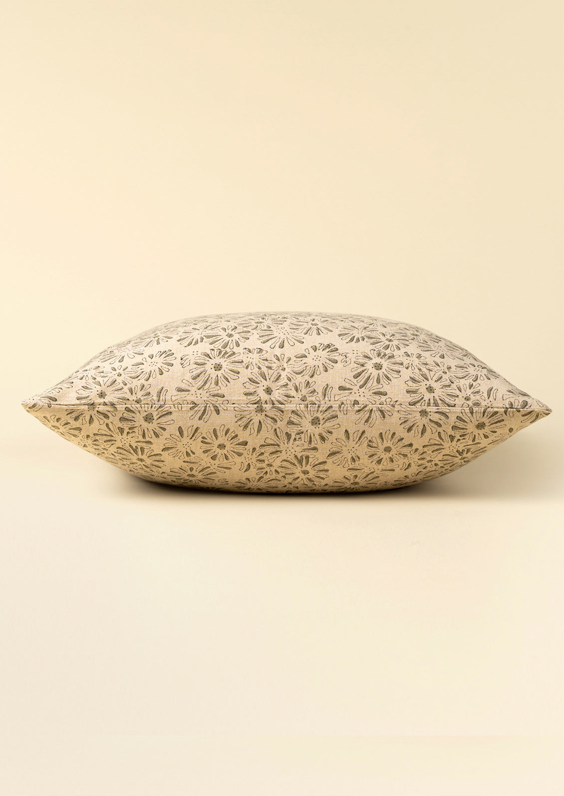 A square decorative throw pillow with a beige and gray floral laser-cut pattern, shown against a solid cream background.