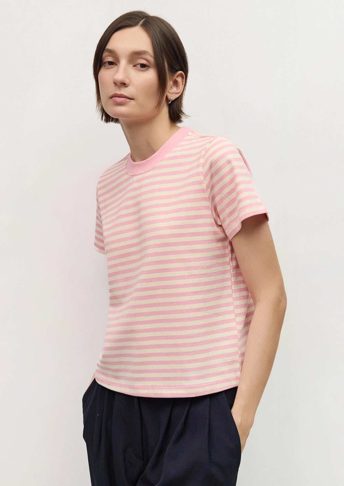 A woman wearing a light pink and white striped short-sleeve t-shirt with a solid pink crew neck.