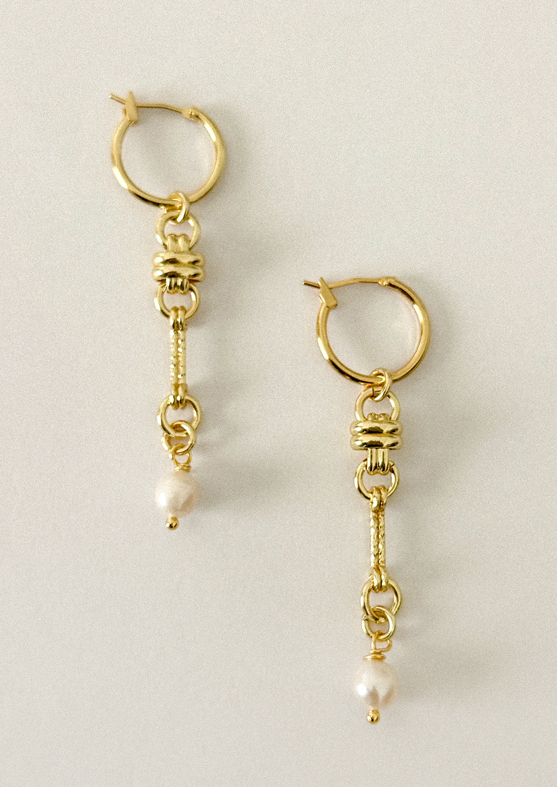 A pair of gold hoop earrings with dangling chain links and small white pearl beads, shown on a plain light beige background.