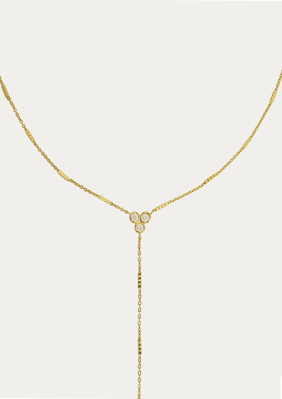 A delicate gold Y-necklace featuring a central cluster of three small round clear stones, photographed against a solid off-white background.