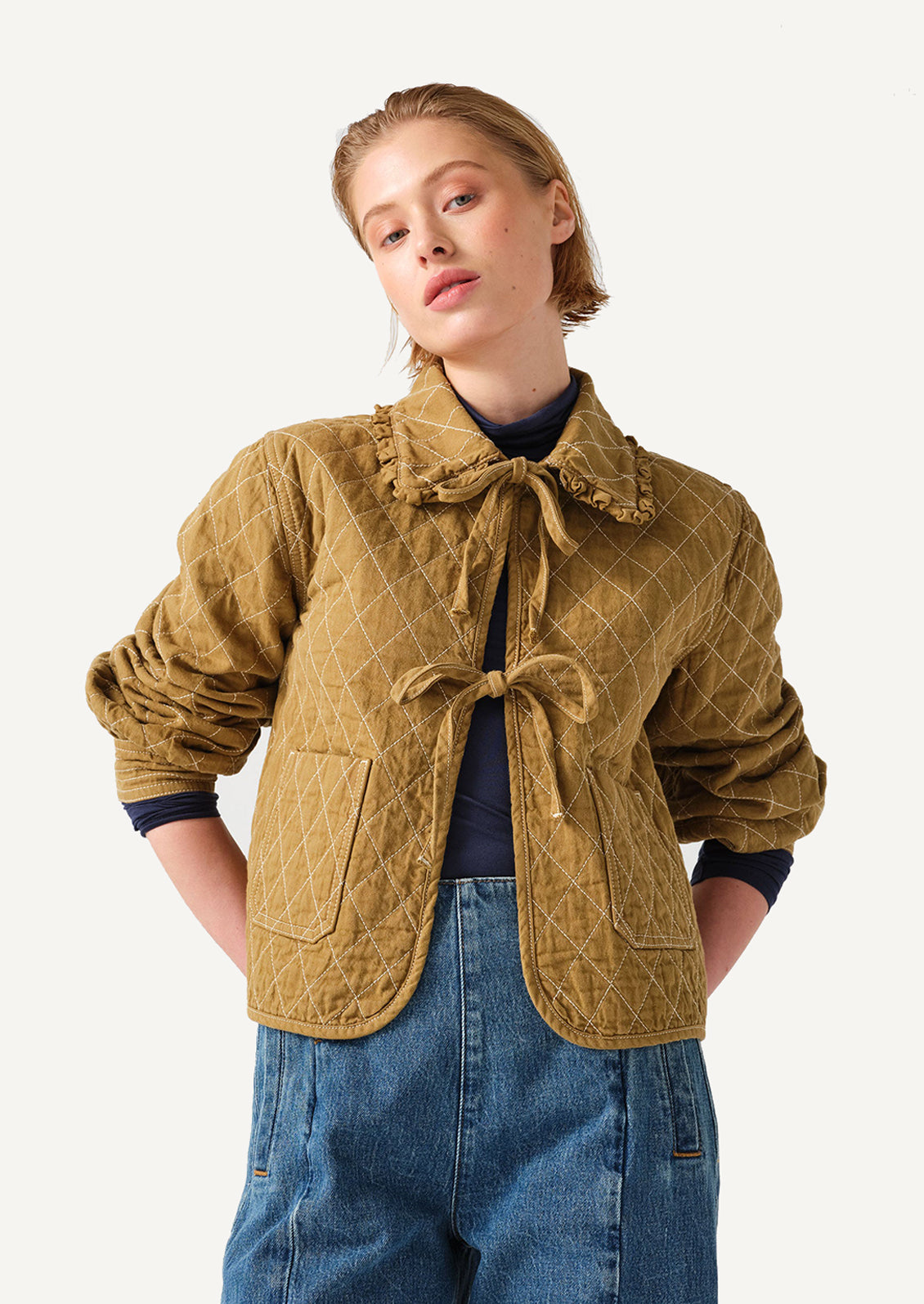 A woman wearing an ochre colored jacket with diamond quilting and bow tie front.