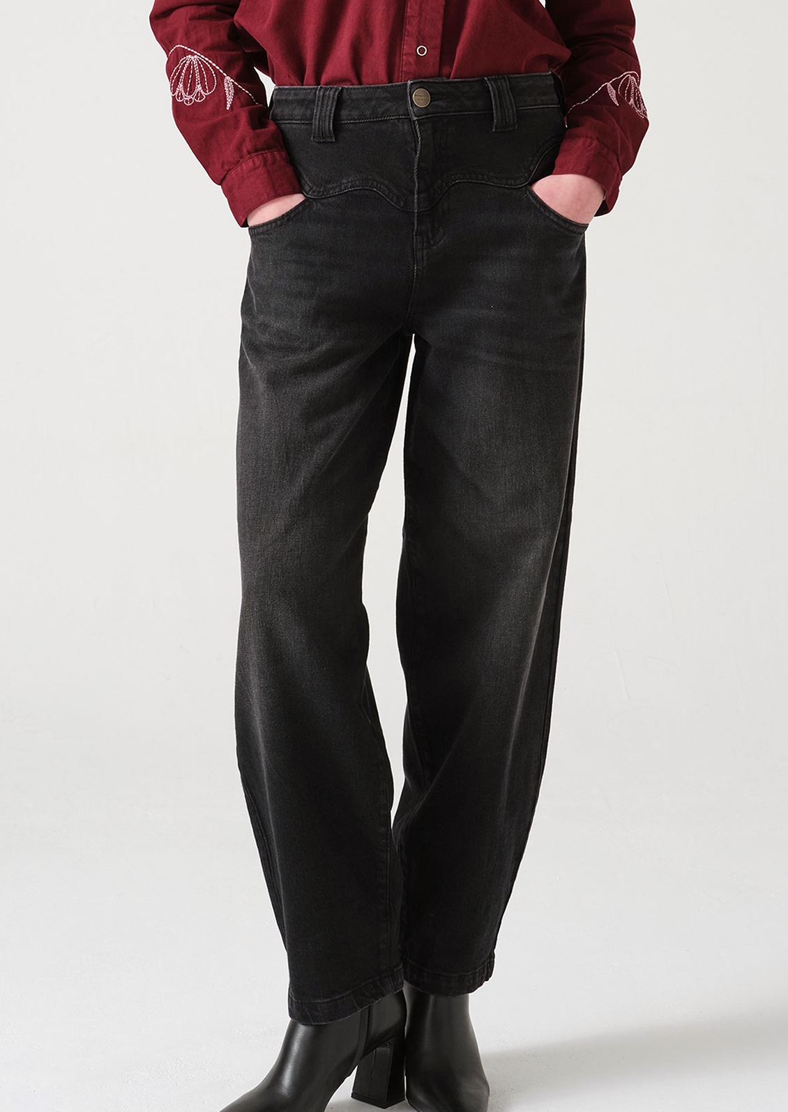 A woman wearing a pair of dark grey barrel leg jeans with decorative yoke detailing.