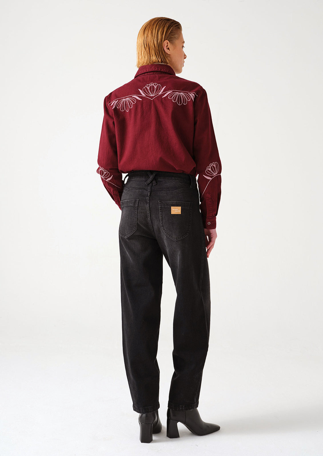 A woman wearing a pair of dark grey denim barrel leg jeans with decorative yoke detailing.